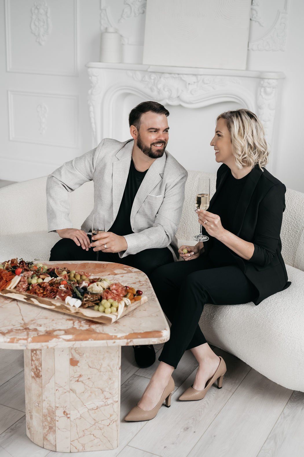 A couple sitting on a couch while enjoying champagne and a charcuterie board