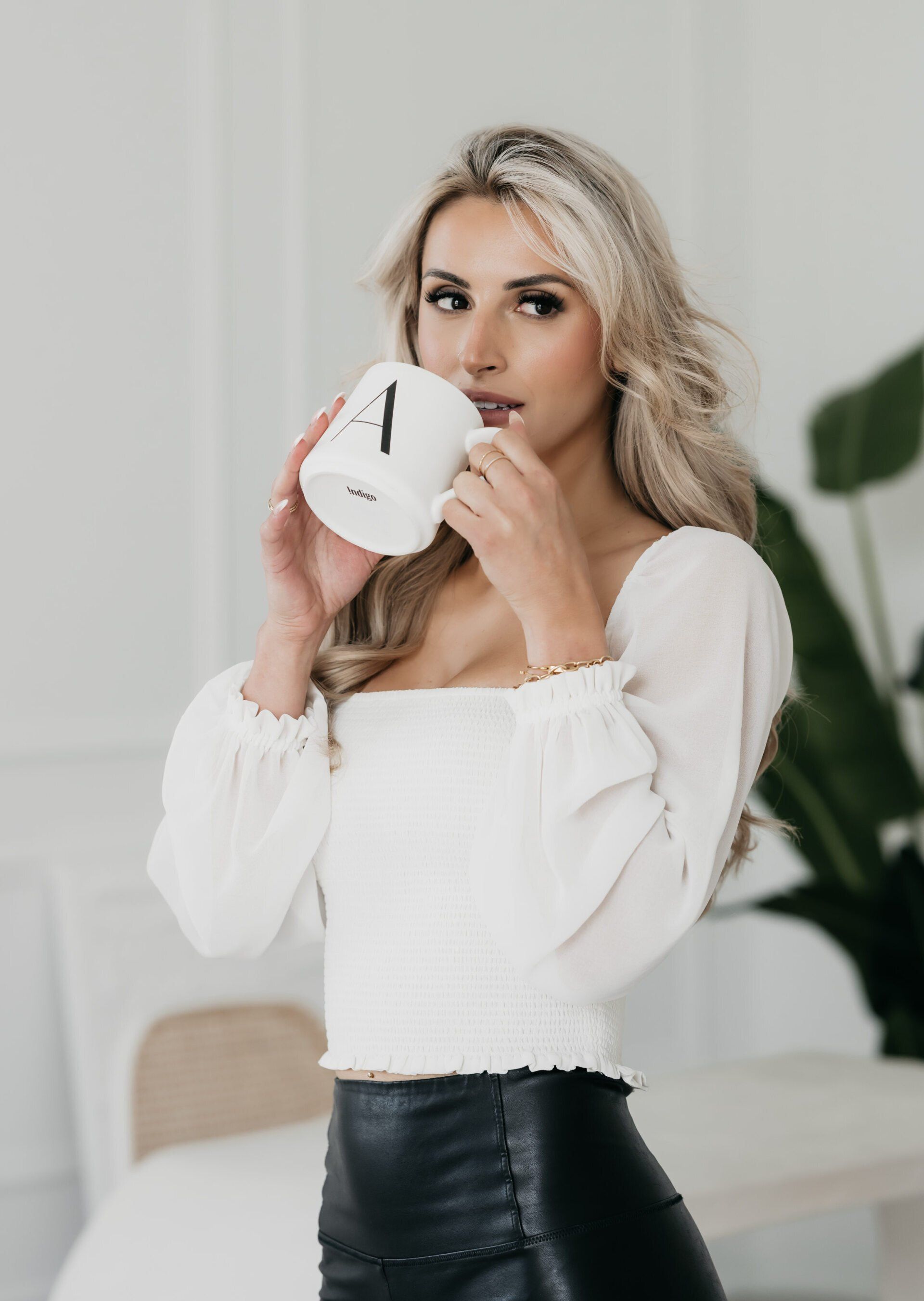 A woman in a white top and black pants is drinking a cup of coffee.