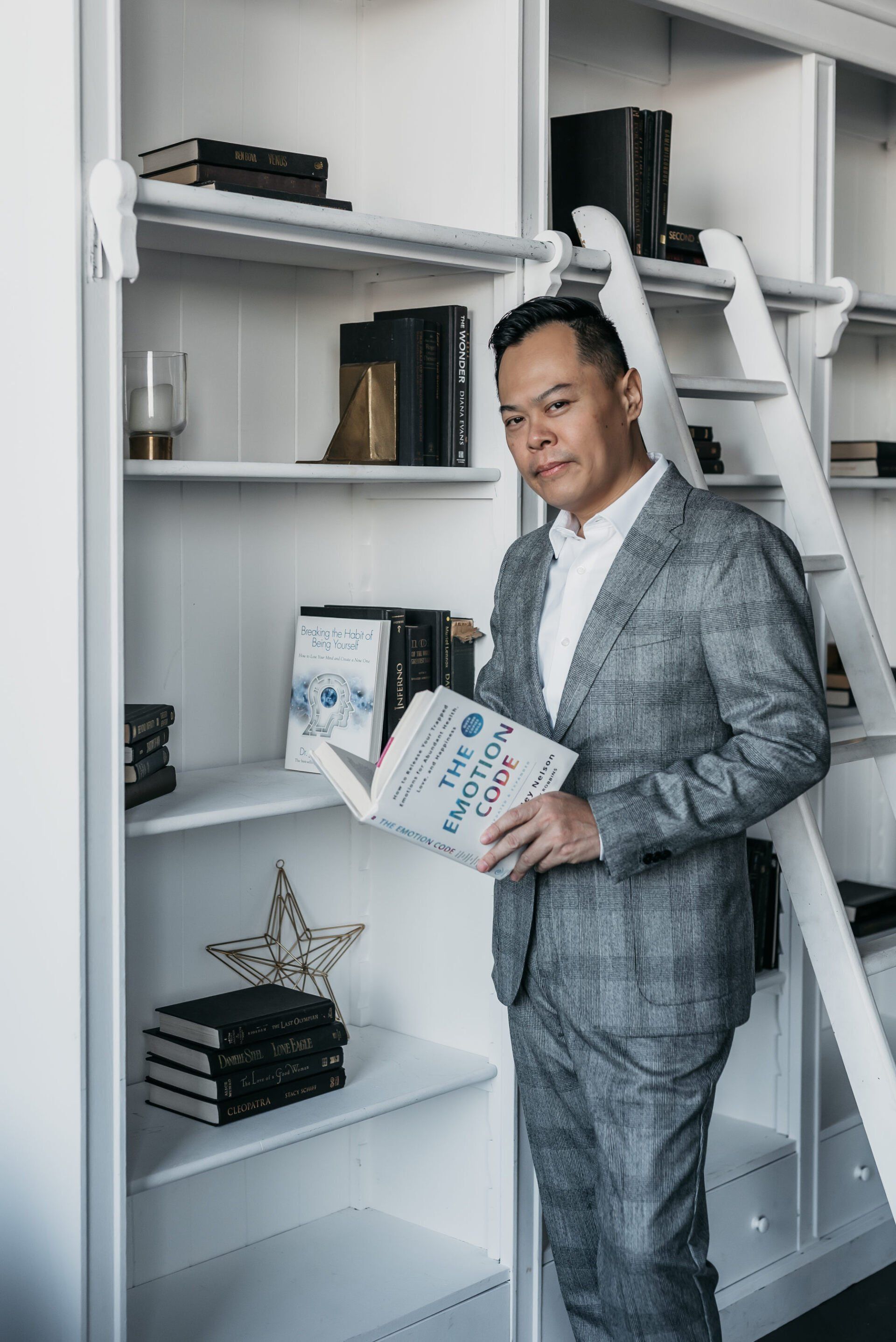 Personal branding photo of a man in a grey suit holding a book beside book shelves