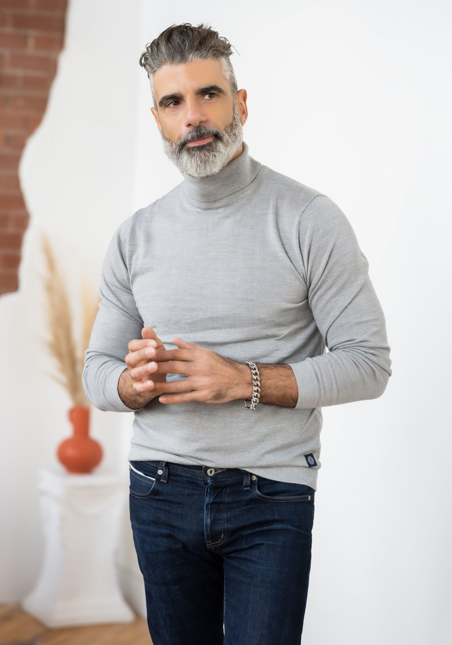 A man wearing a grey turtle neck sweater and jeans for his professional LinkedIn headshot.