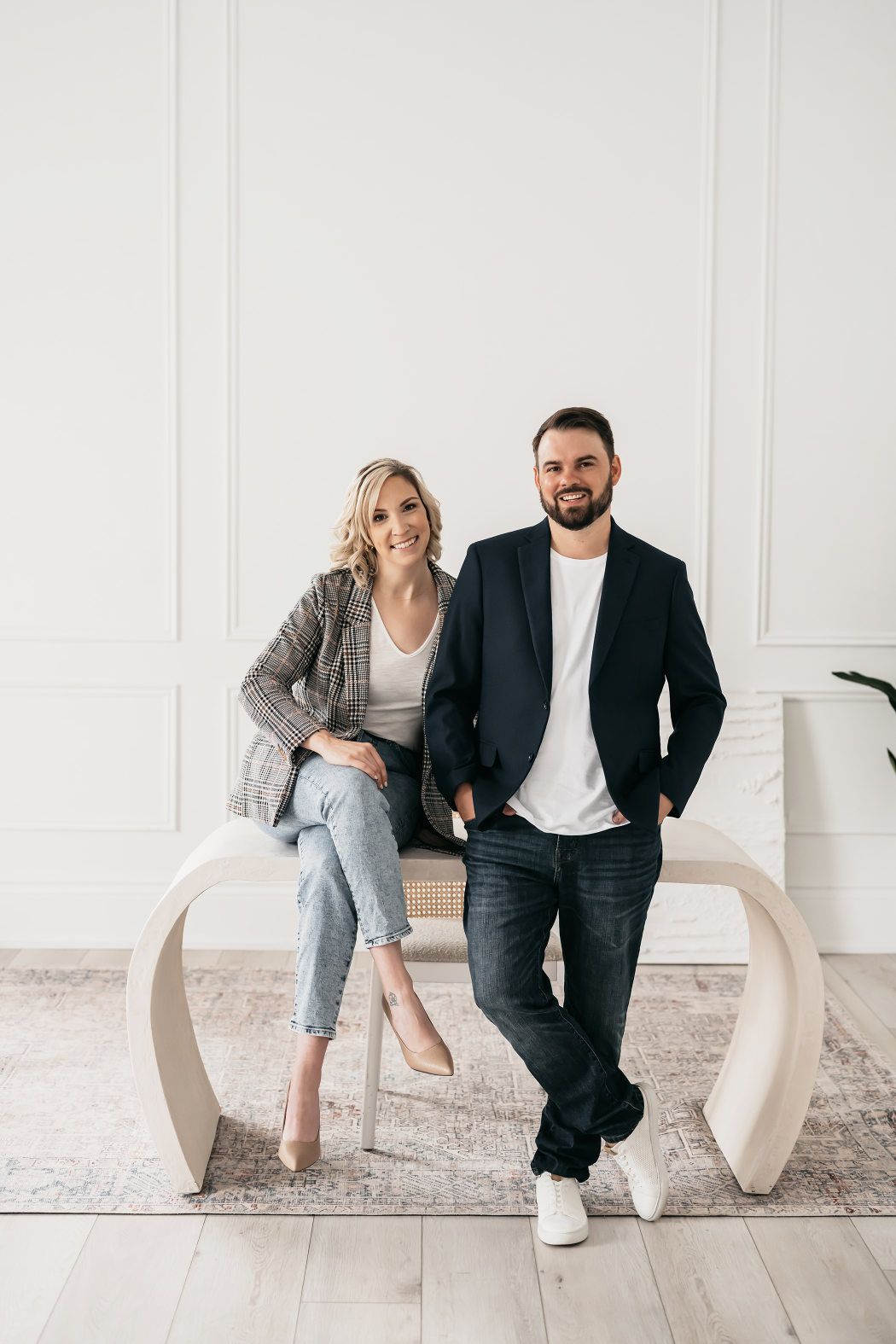 A man and woman posing on a bench during a branding photoshoot in a white room.