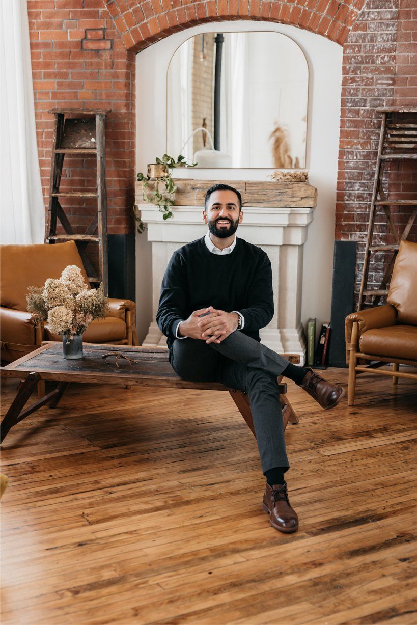 A man wearing a smart casual outfit as he sits on a rustic center table in the middle of a cabin aesthetic living room setup