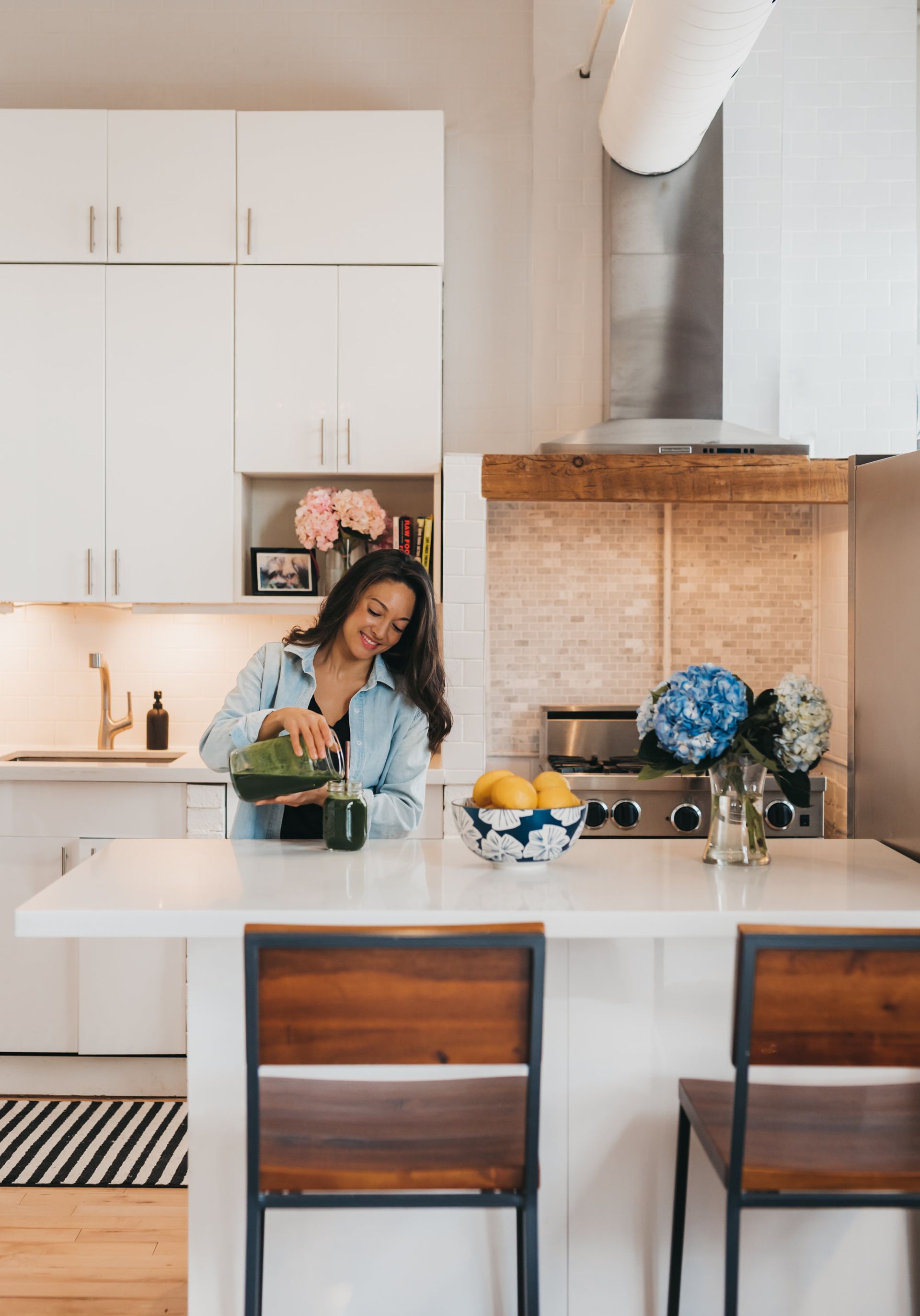 A woman is pouring a drink into a cup in a kitchen.