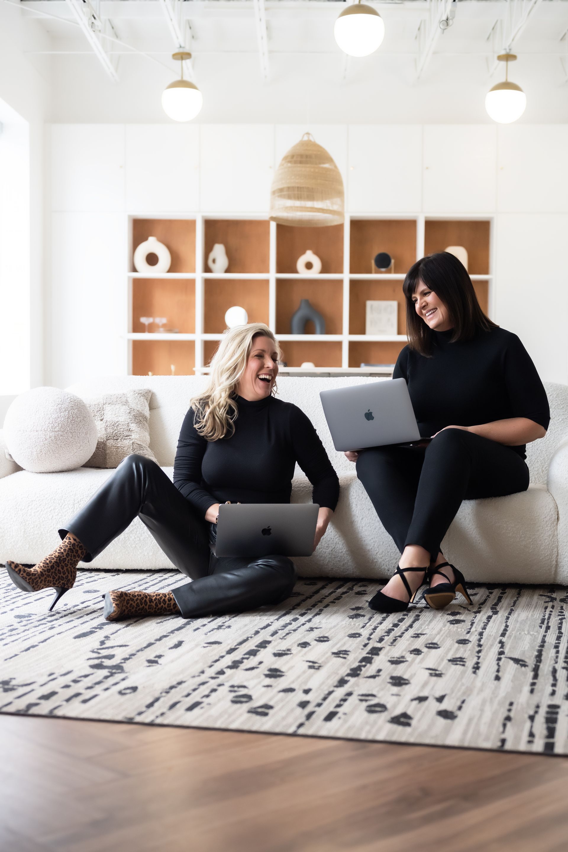 two realtors smiling at each other while using their laptops