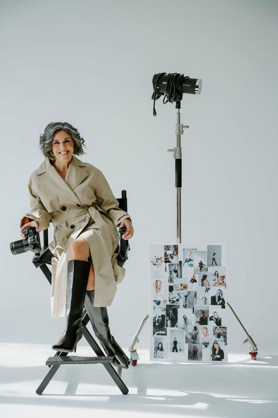 Stacey Naglie is sitting in a director 's chair holding a camera.