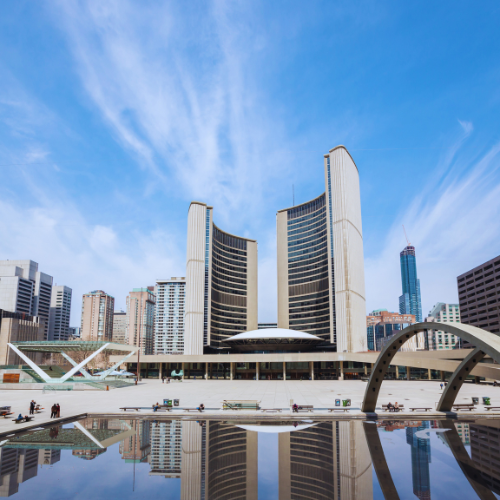 Modern twin-tower building with a curved design, reflecting in a large pool under a clear blue sky.