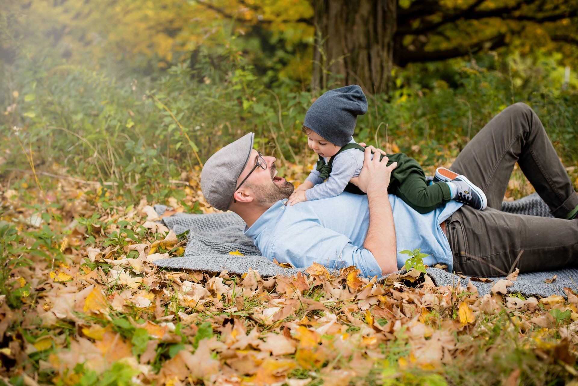 Photo of a father laying in a leaf covered field while holding a toddler on his stomach