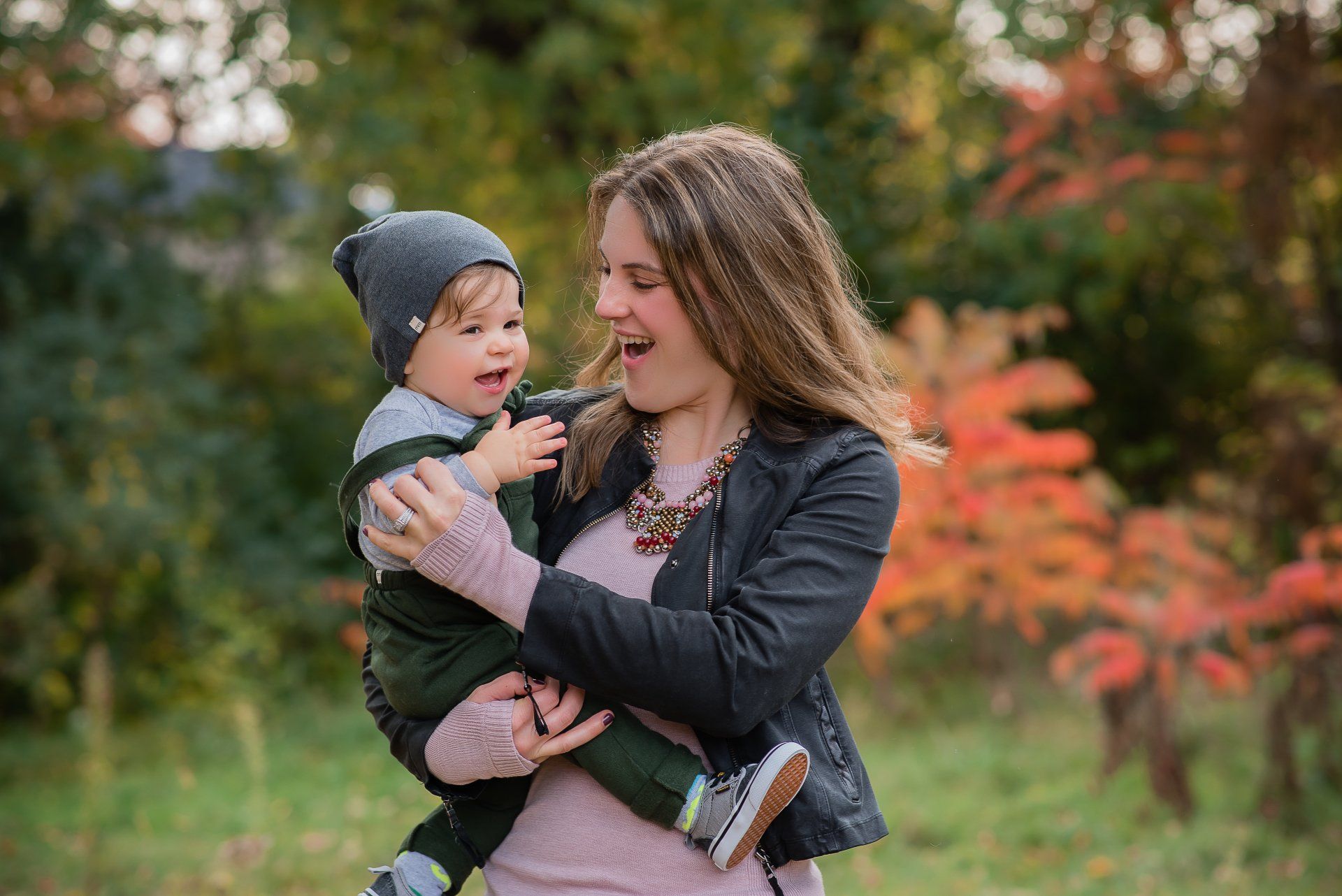Family photo of mother holding toddler with fall foliage in background