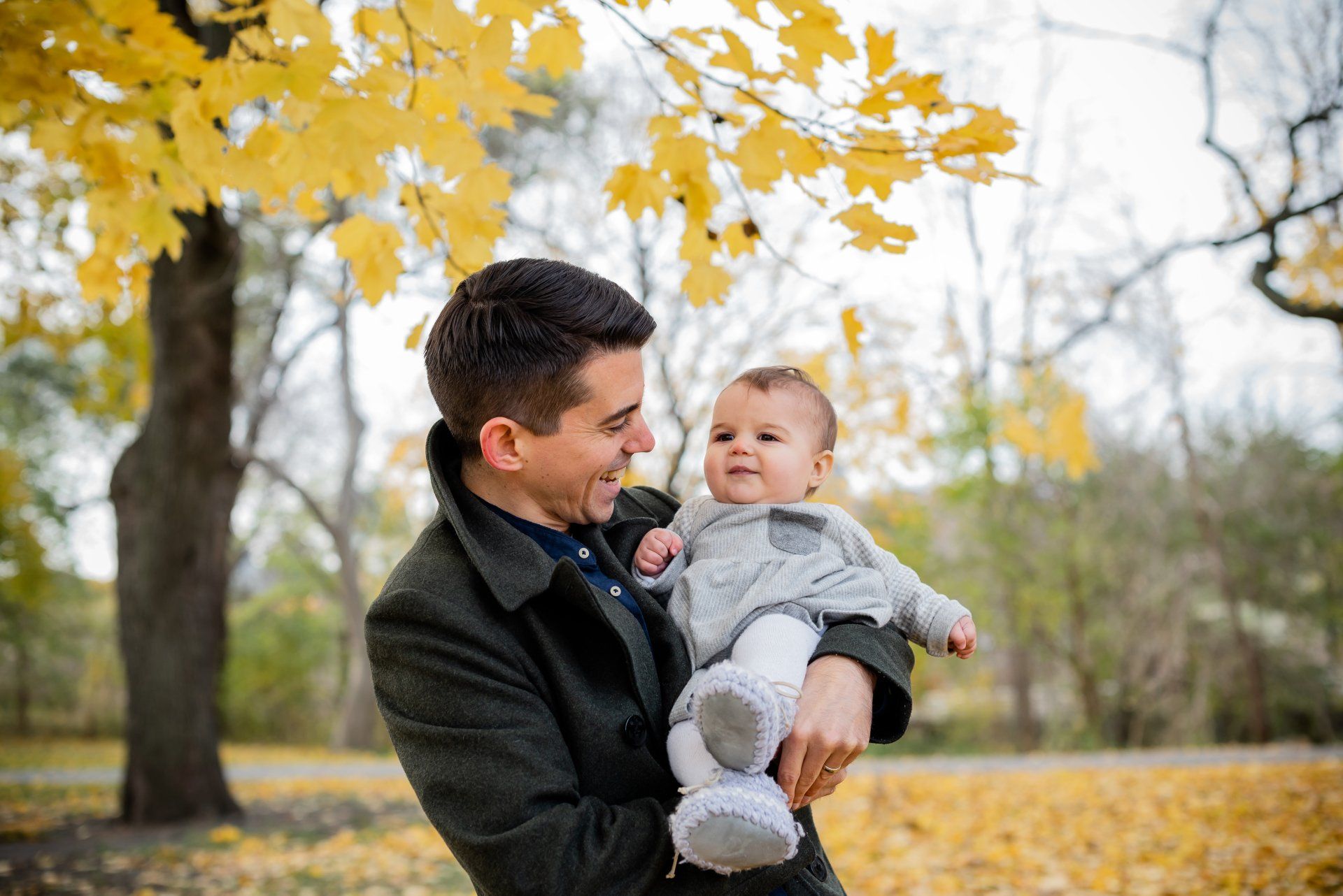 Photo of a father holding a baby while standing in front of a leaf covered field