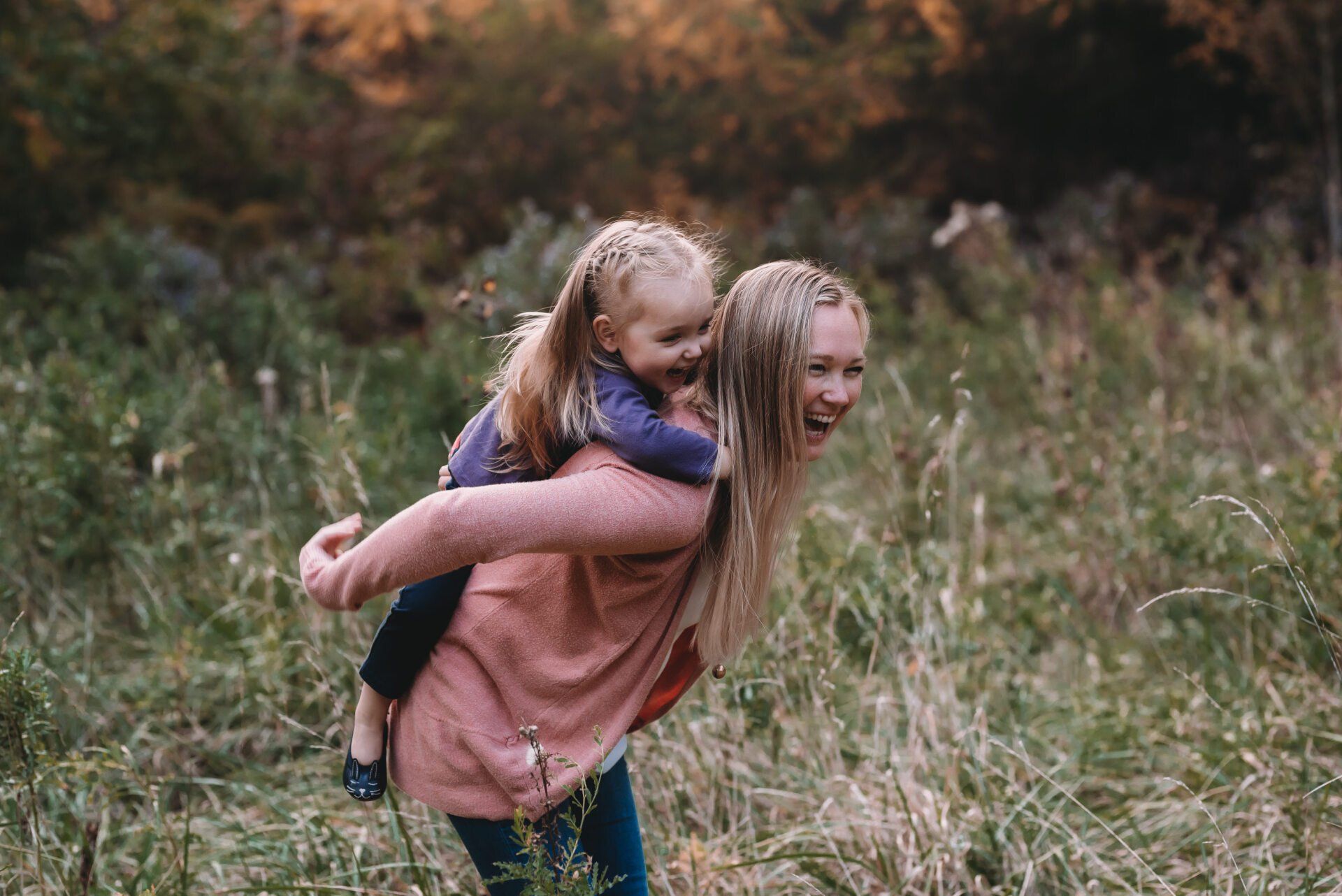 Older sister carrying younger sister on her back while standing in field for fall family photoshoot