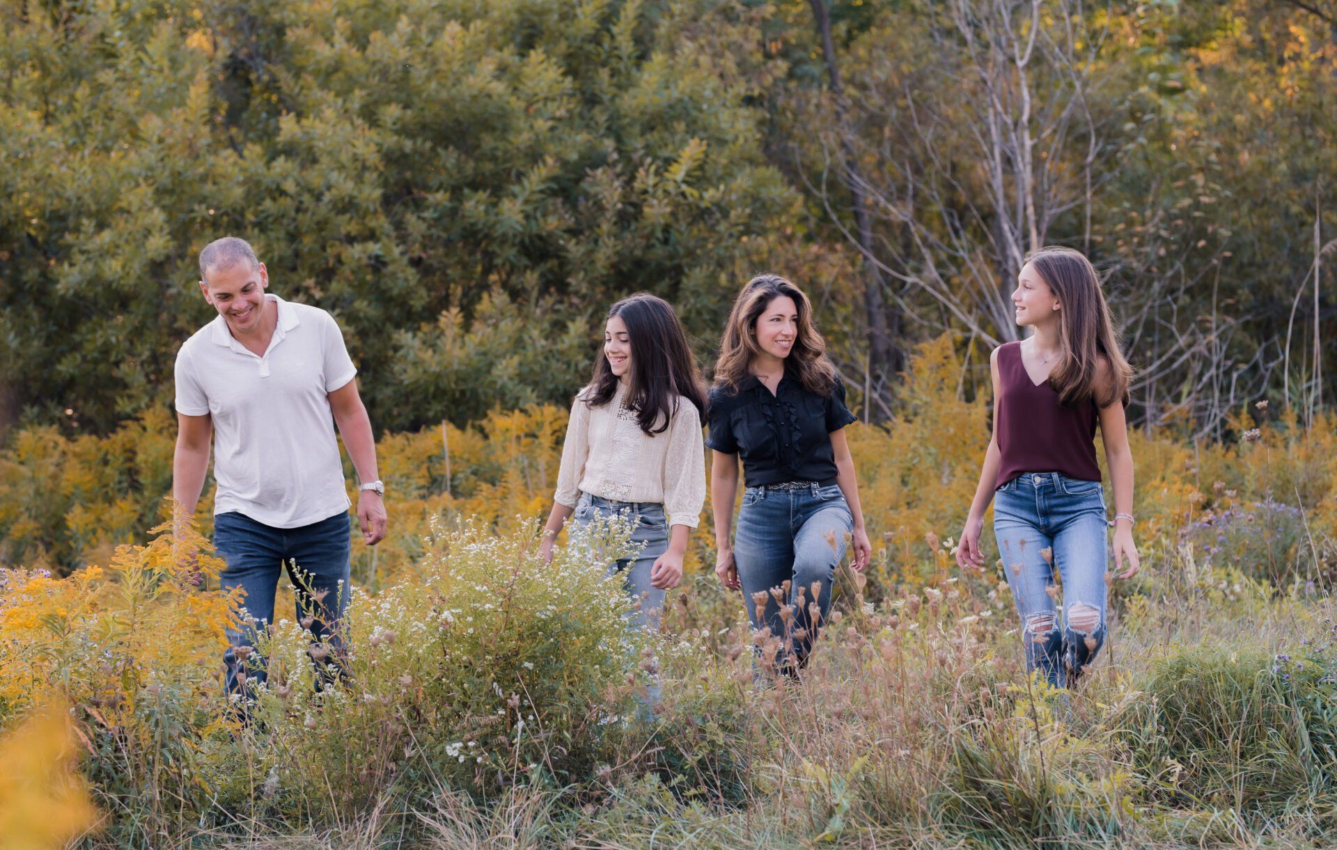 Father, mother and two daughter walking in field for fall photoshoot