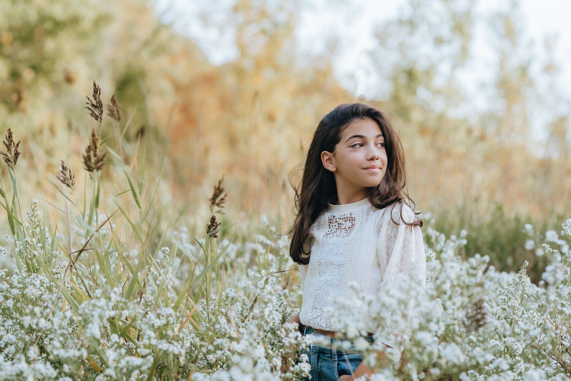 Young girl standing in field of white wild flowers for fall photoshoot