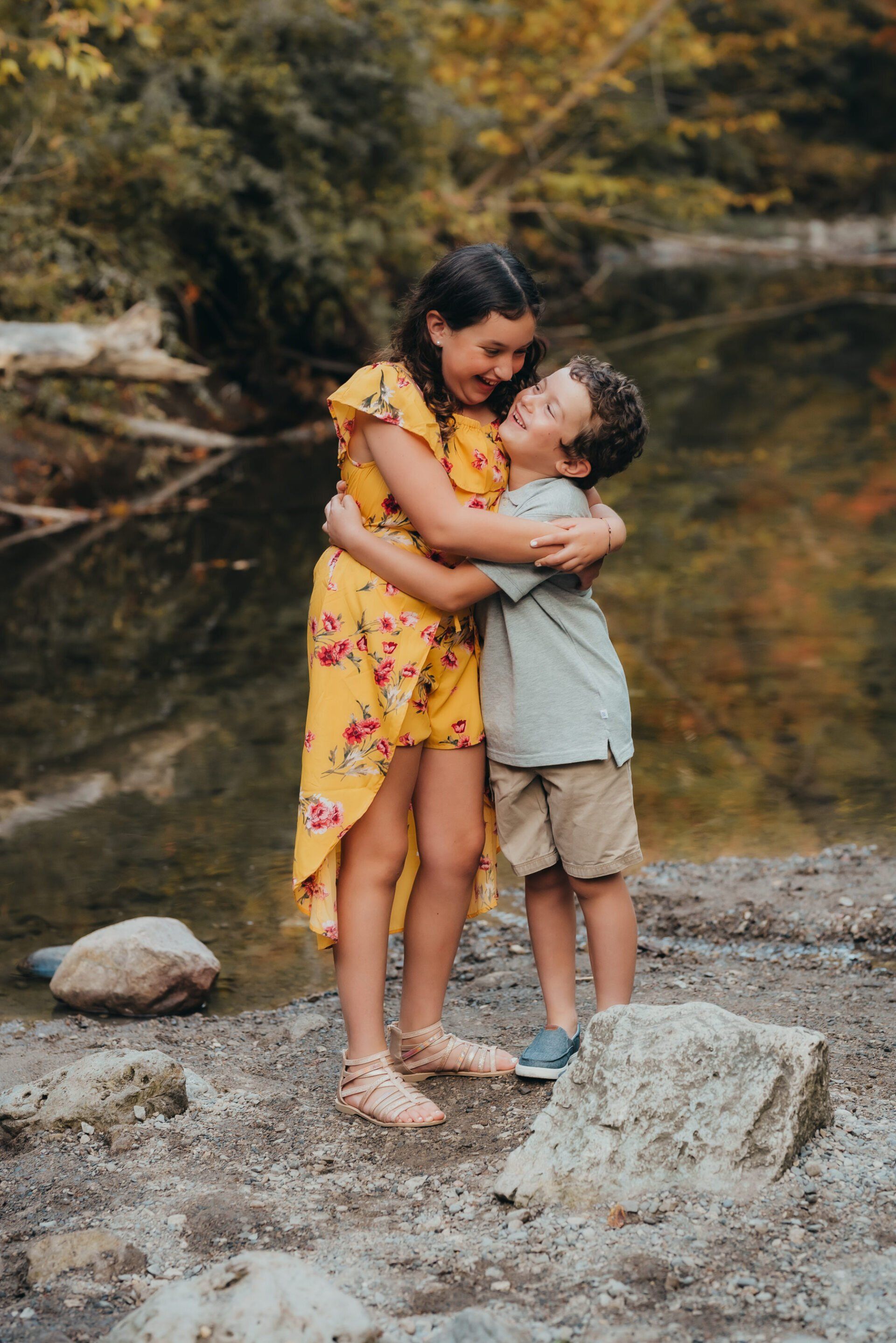 Brother and sister holding on to each other while standing on edge of creek for fall family photoshoot