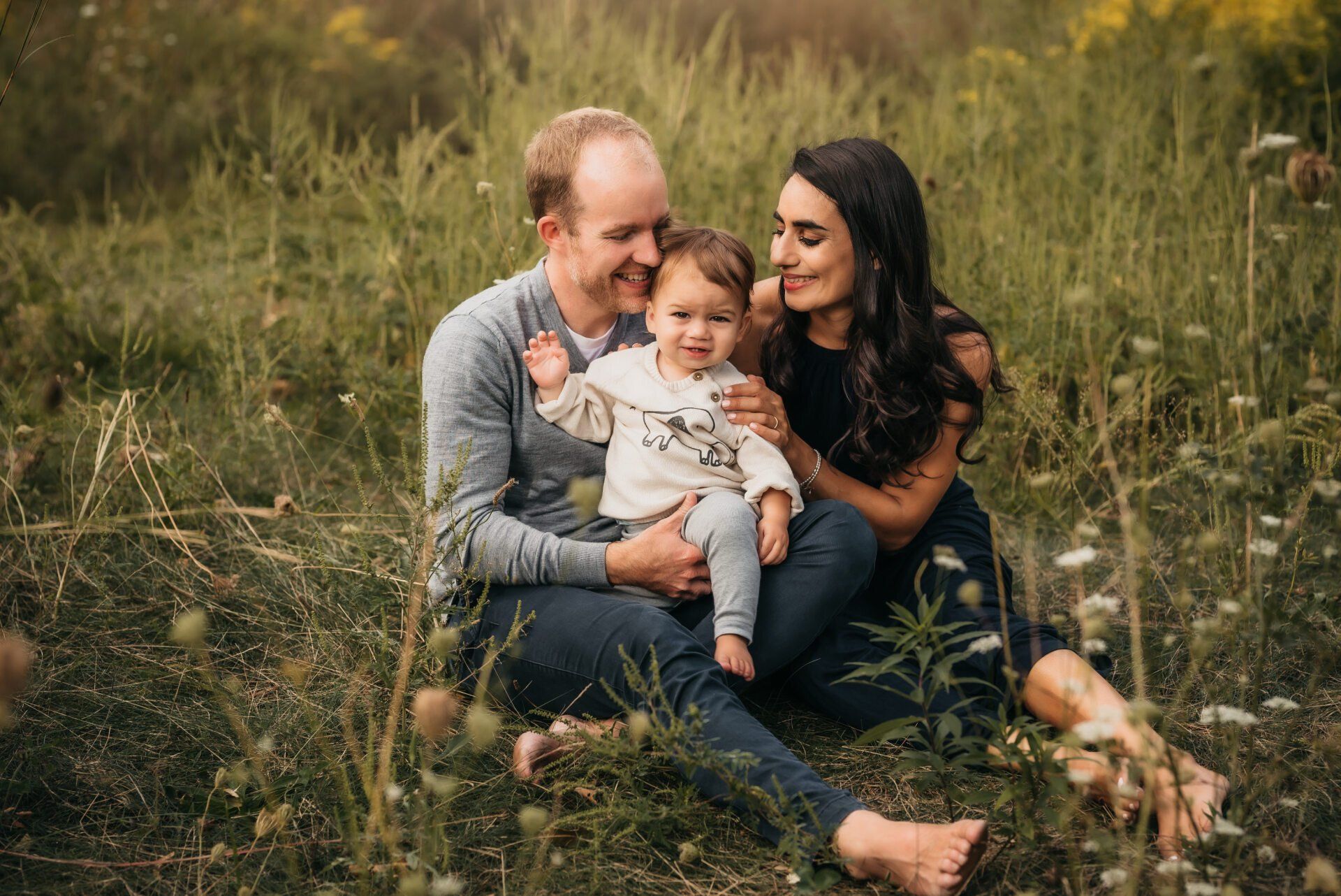 Mother, father and toddler sitting in field for fall family photoshoot