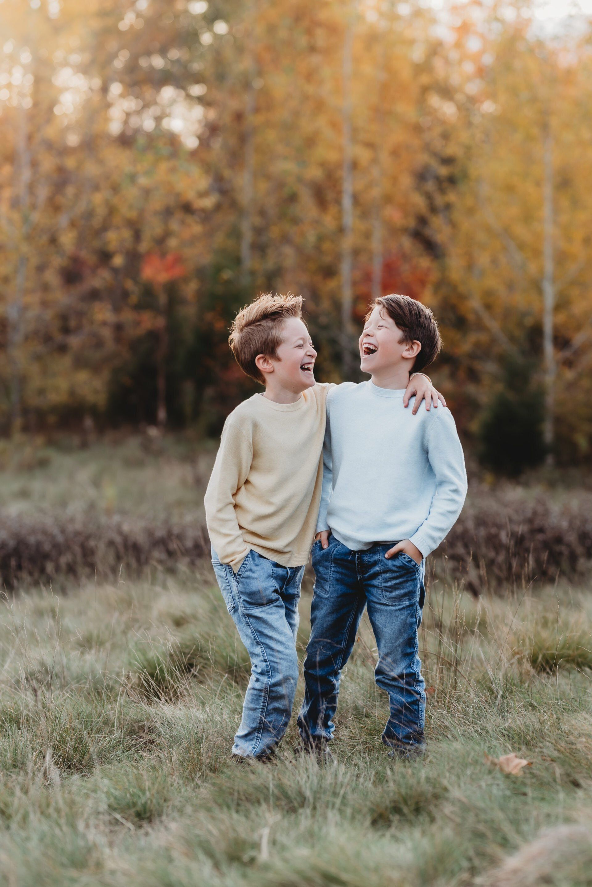 Photo of two brothers with arms over each other's shoulder while walking through grassy field for family photography