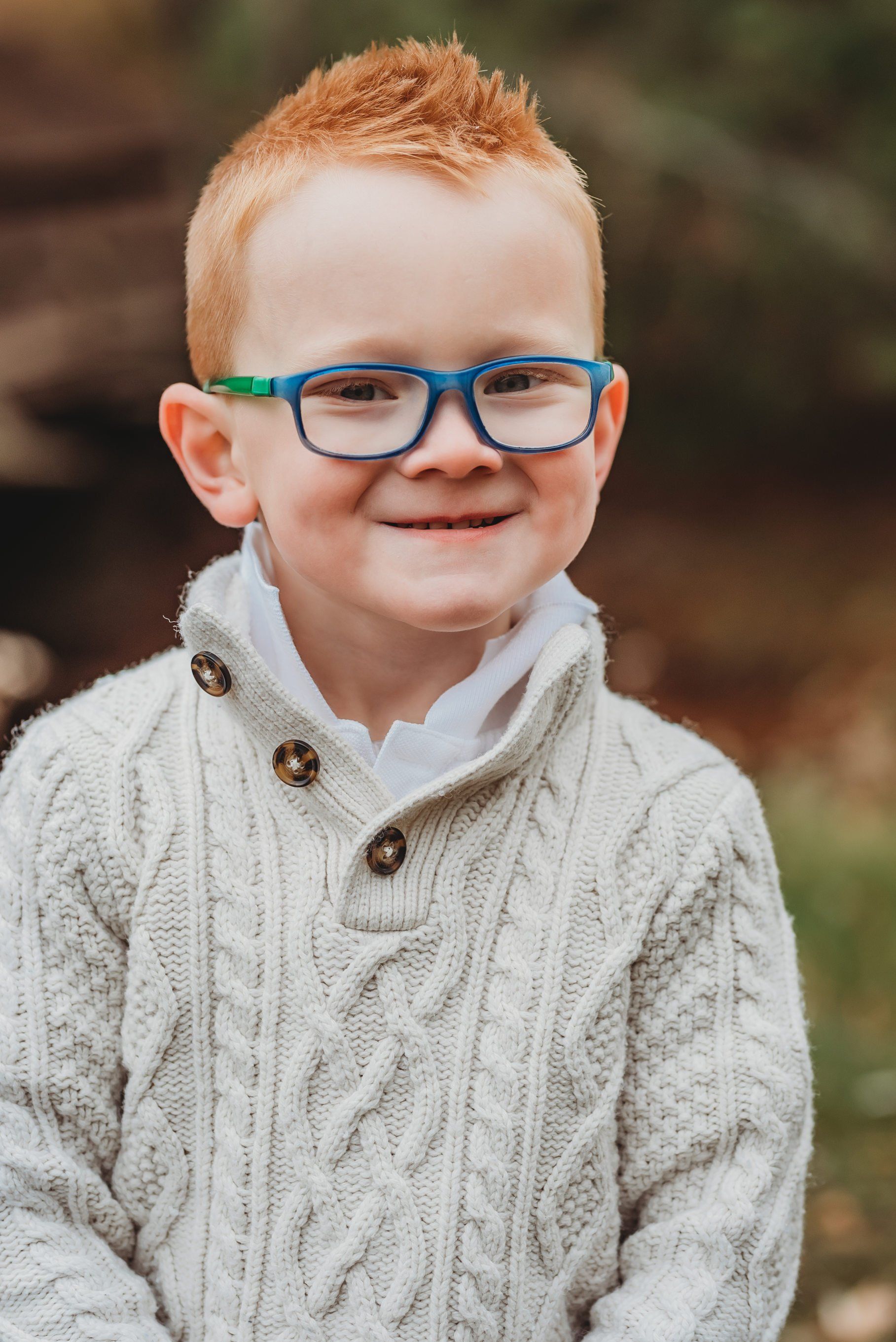 Photo of a small boy smiling while standing outdoors for family photography