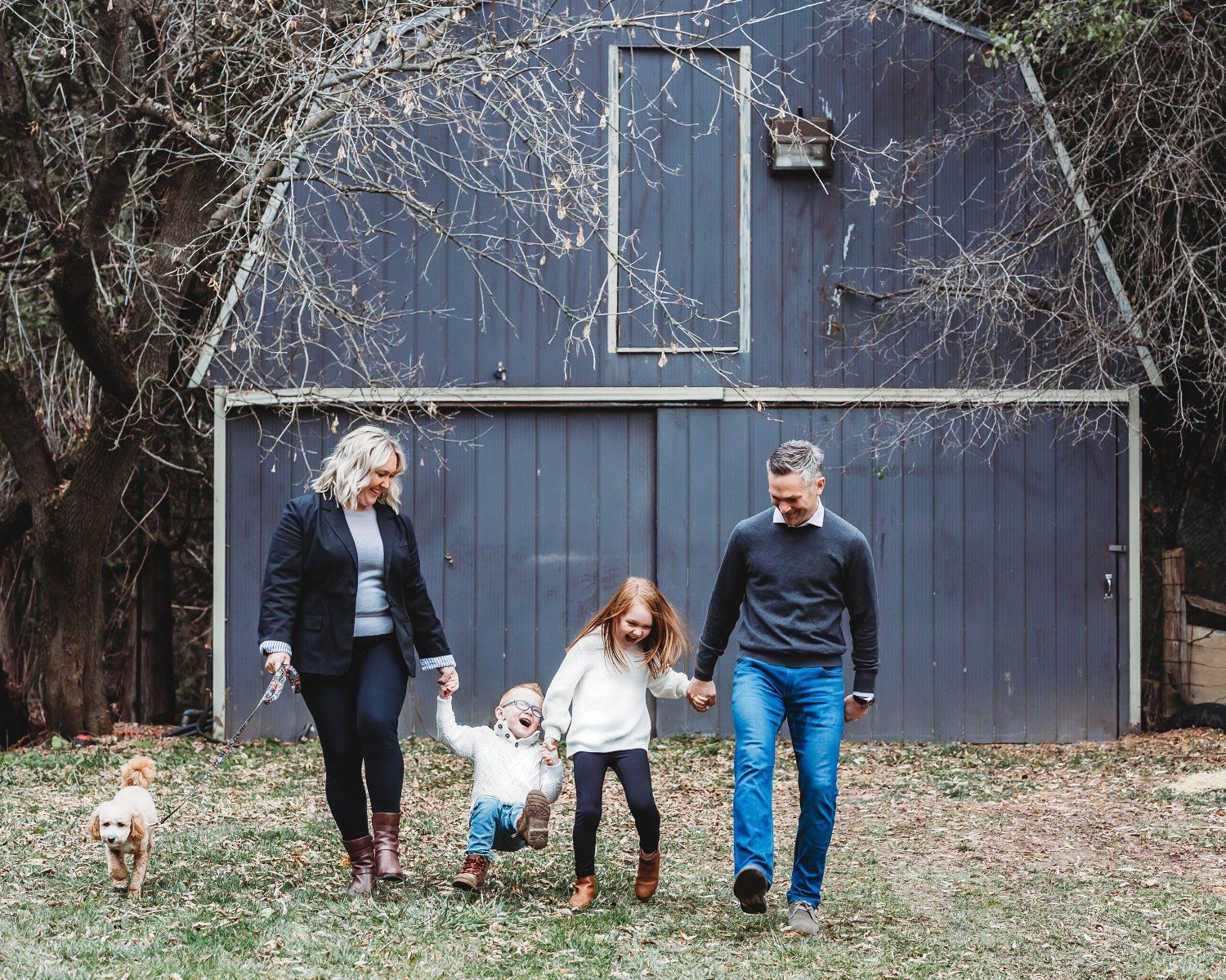 Photo of a Toronto family with small children holding hands while walking in front of a barn for family photography