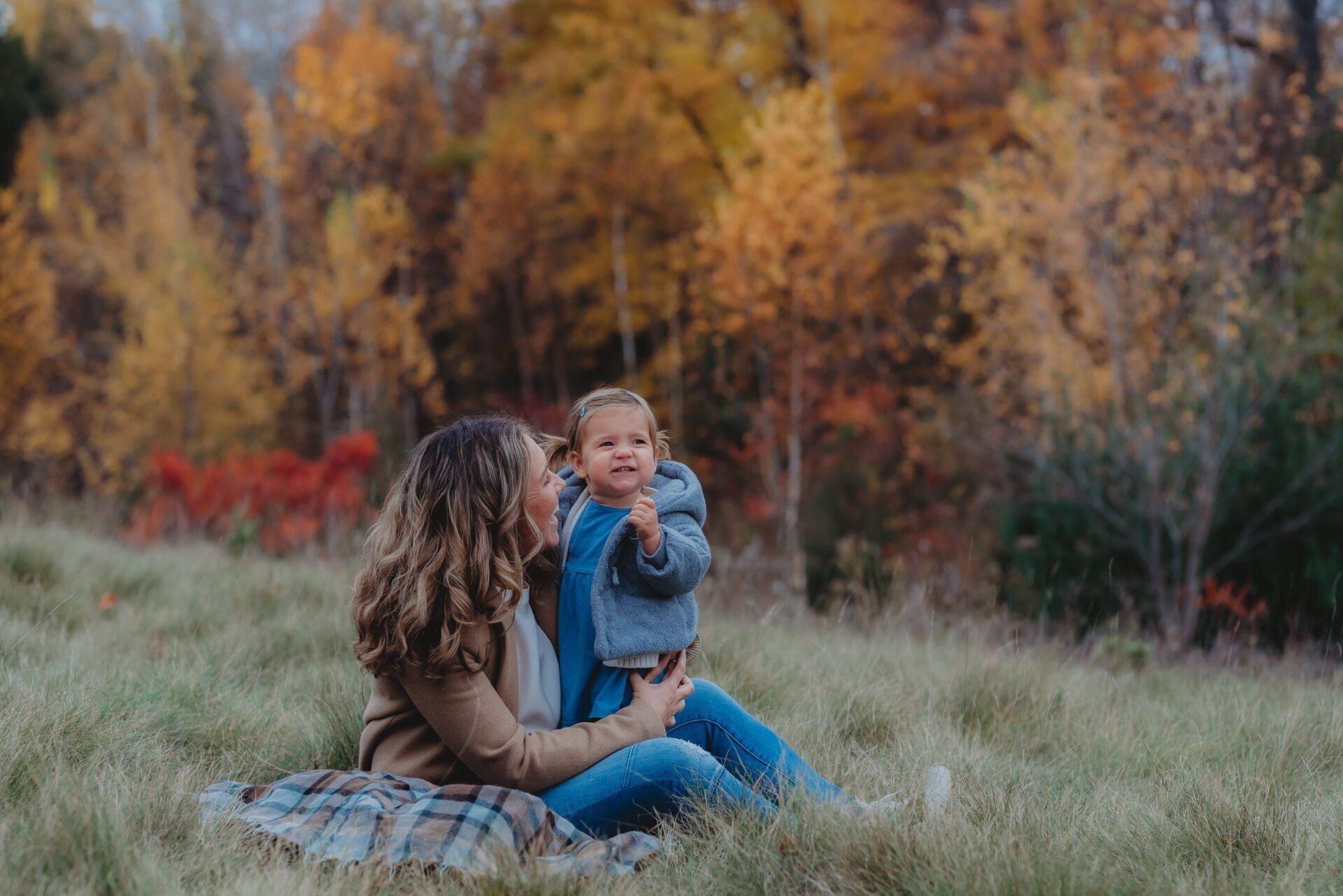 Photo of mom and baby sitting on blanket in grassy field for family photography