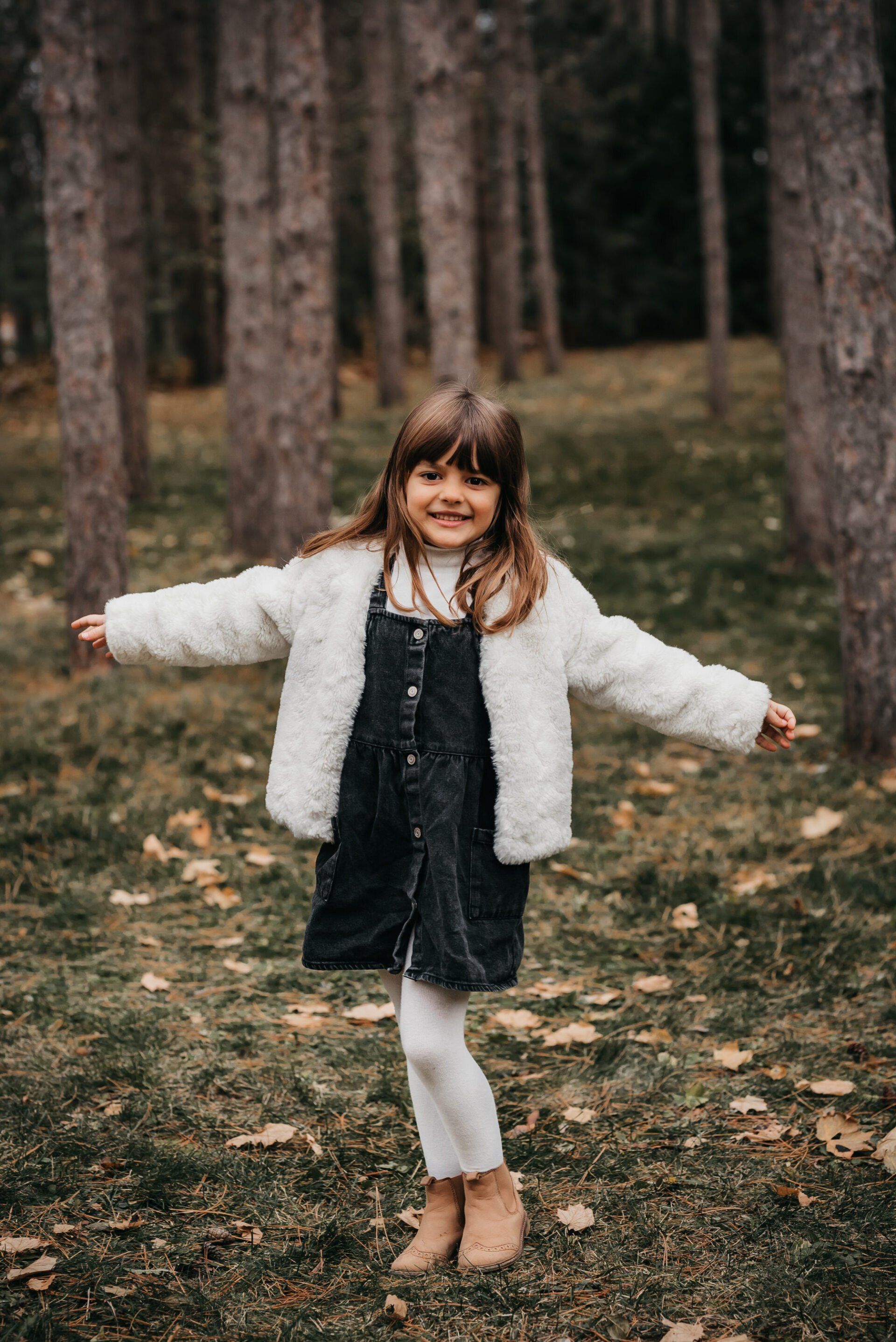 Photo of a small girl with outstretched hands while standing in wooded area for family photography