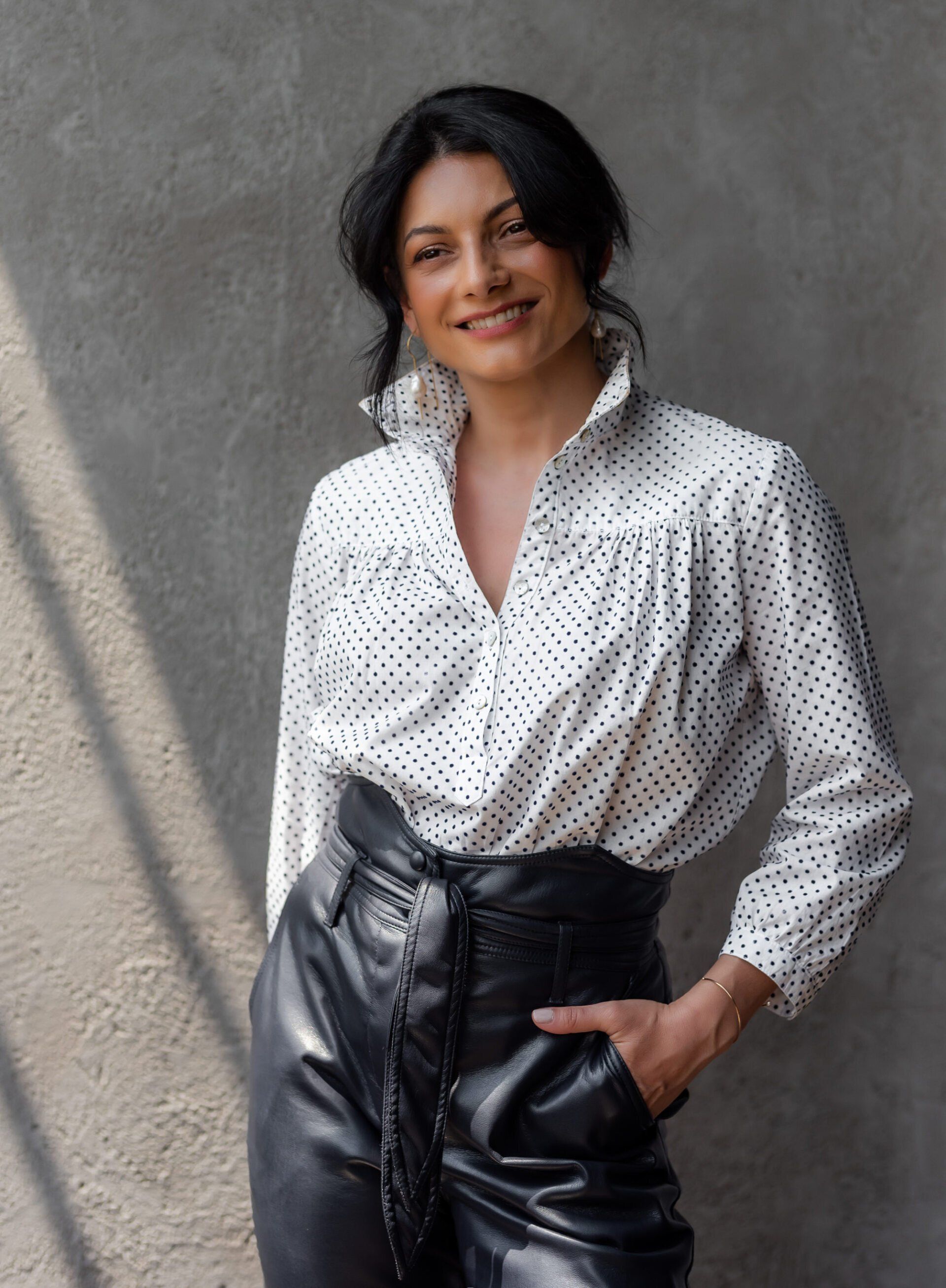 A woman smiles and stands confidently with one hand in her leather pant pocket.