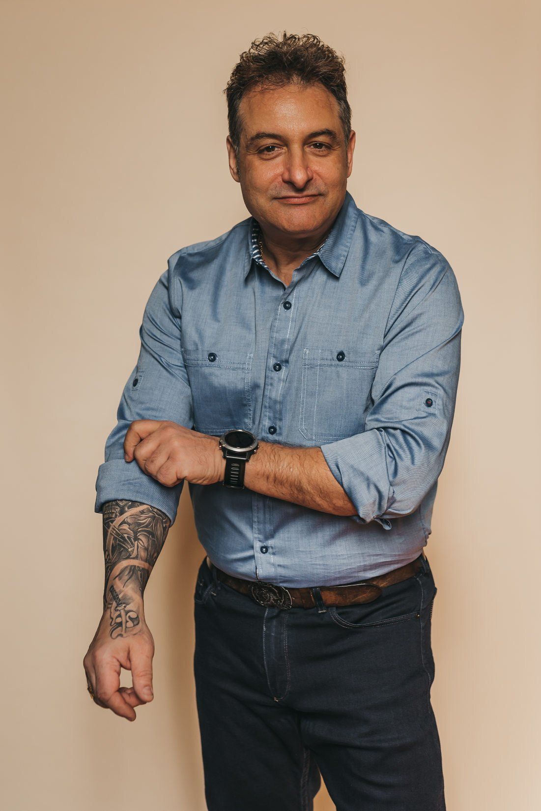 A male business owner rolling up his shirt sleeve exposing a tattooed arm in a professional headshot photo