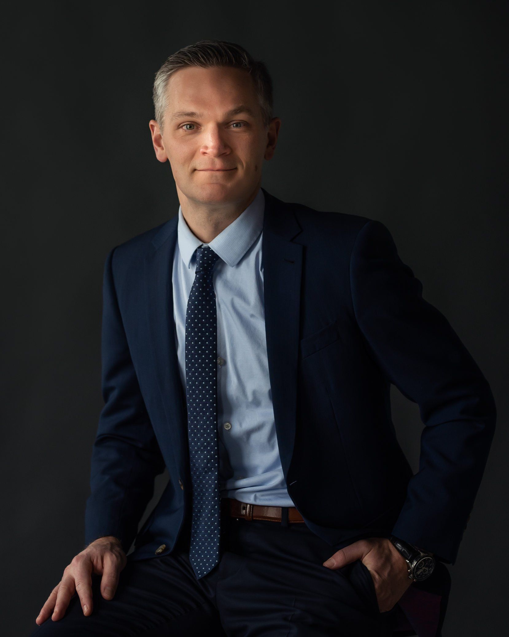 A business executive sitting and wearing a blue suit and tie in a professional headshot picture