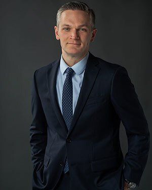 A male business executive wearing a suit and tie in a professional headshot photograph