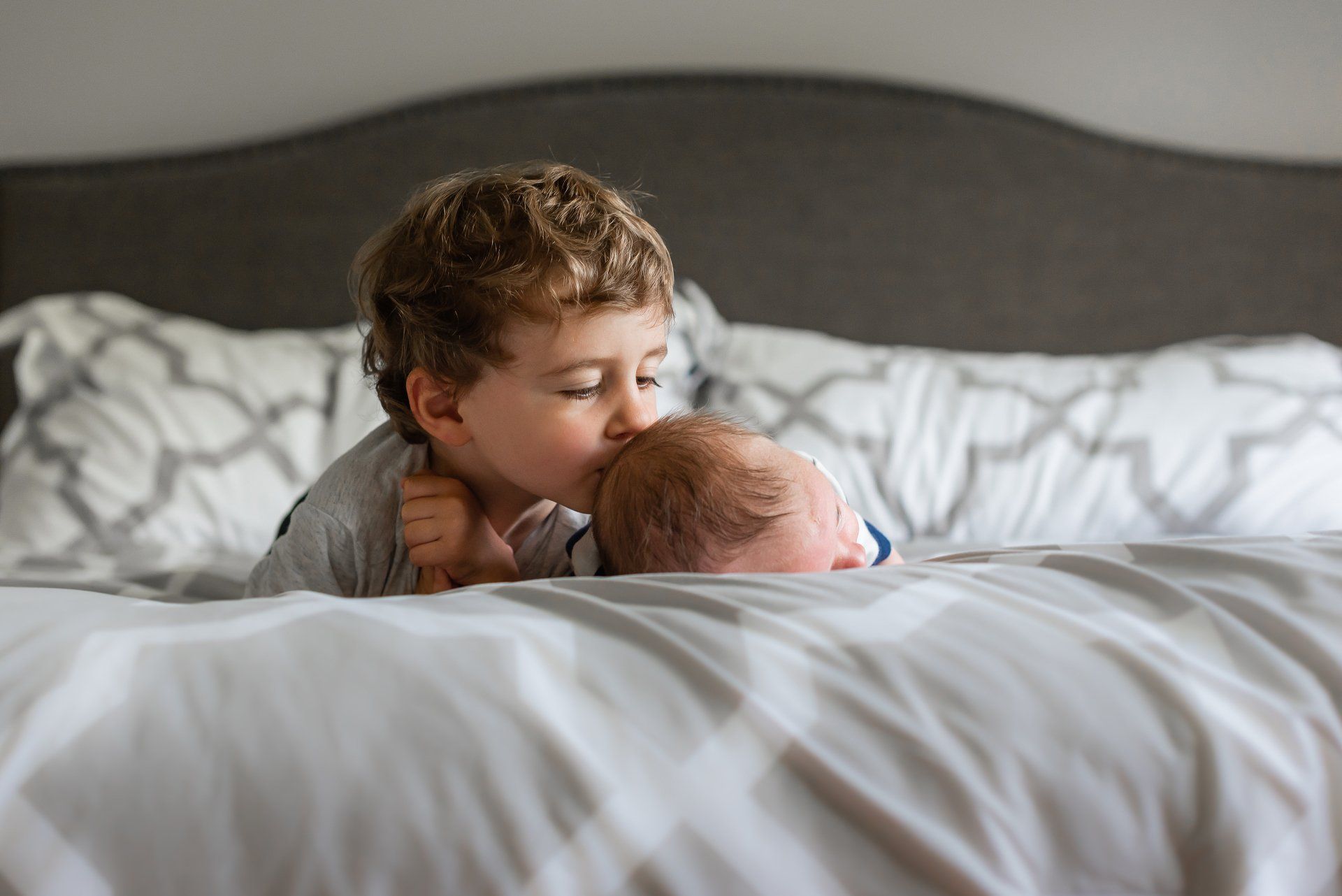 Family photographer Toronto | Stacey Naglie | Toddler kissing newborn on back of head while lounging on bed