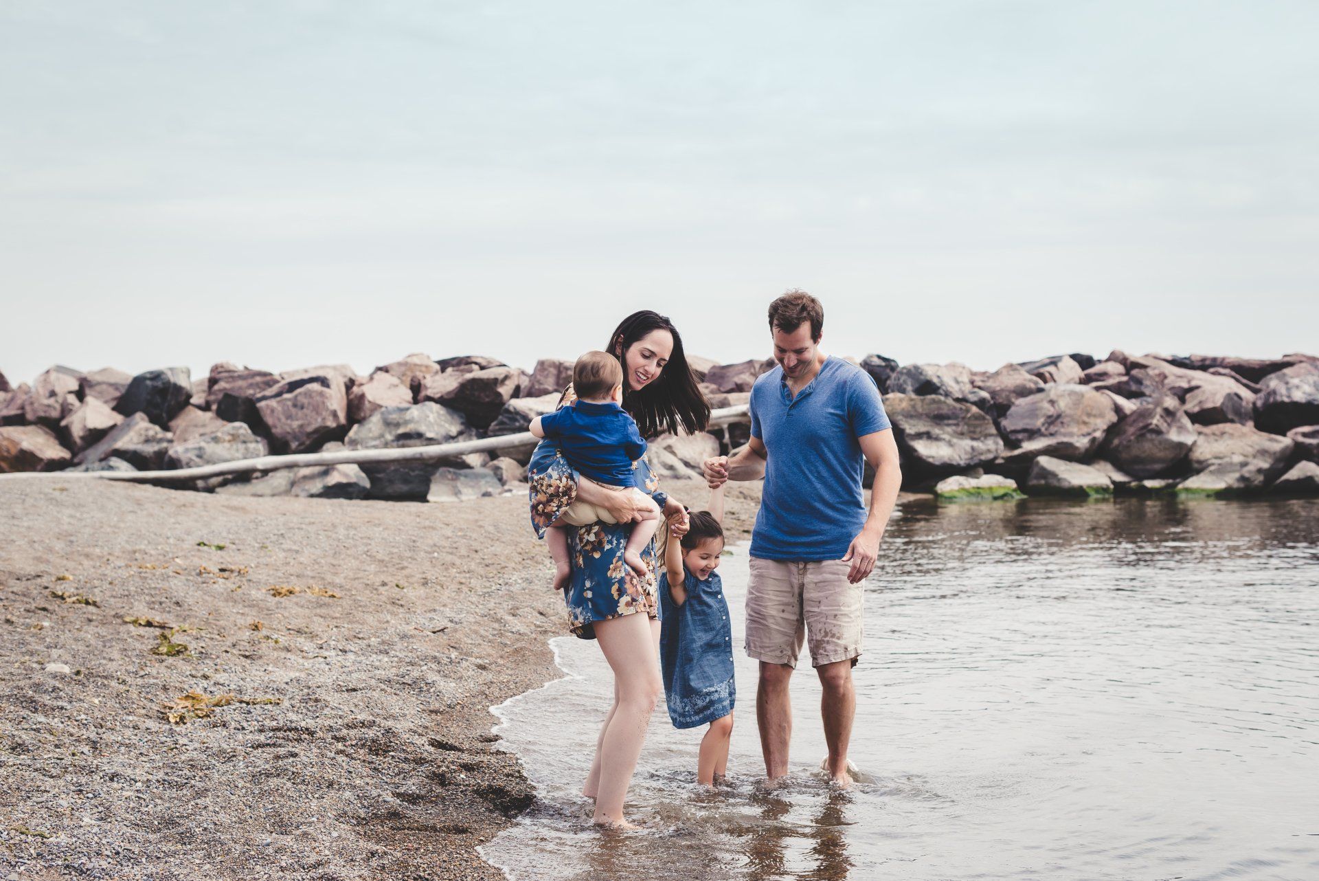Family lifestyle photograph of a mother and father with two children standing at water's edge