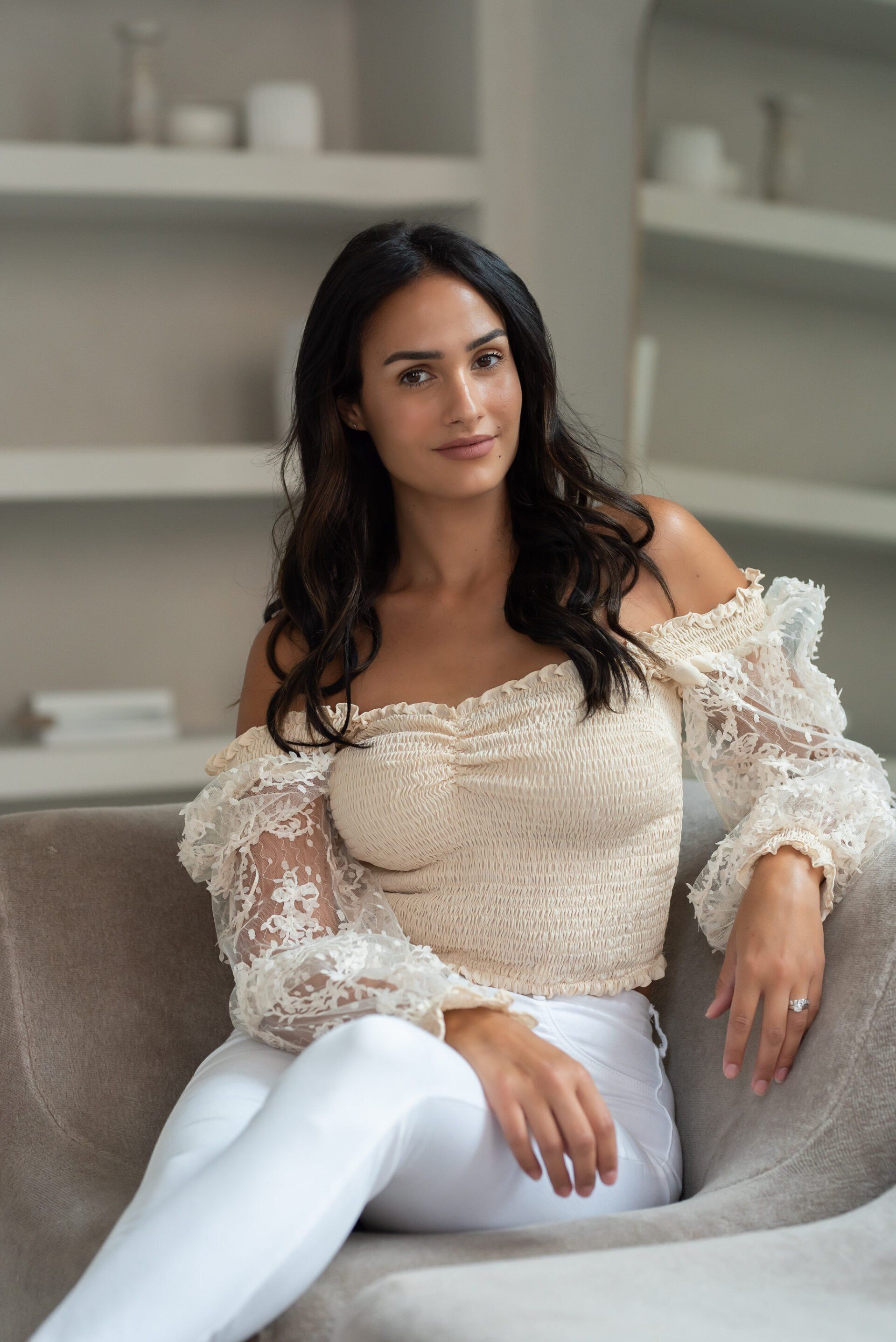 Social media influencer Chantel sitting on a suede sofa with a floral off-shoulder lace top
