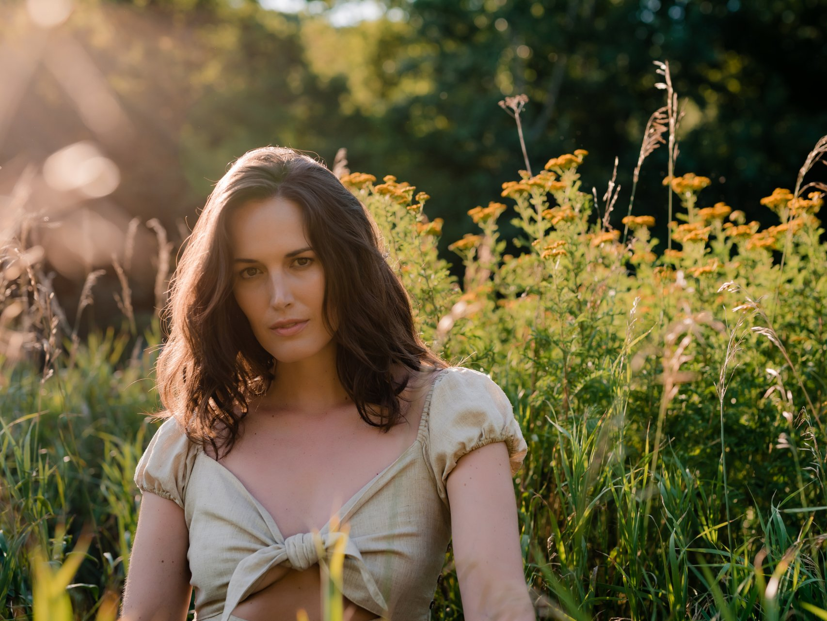Personal branding photo of a woman with brunette hair wearing a halter top while standing in front of field of tall, golden wild flowers