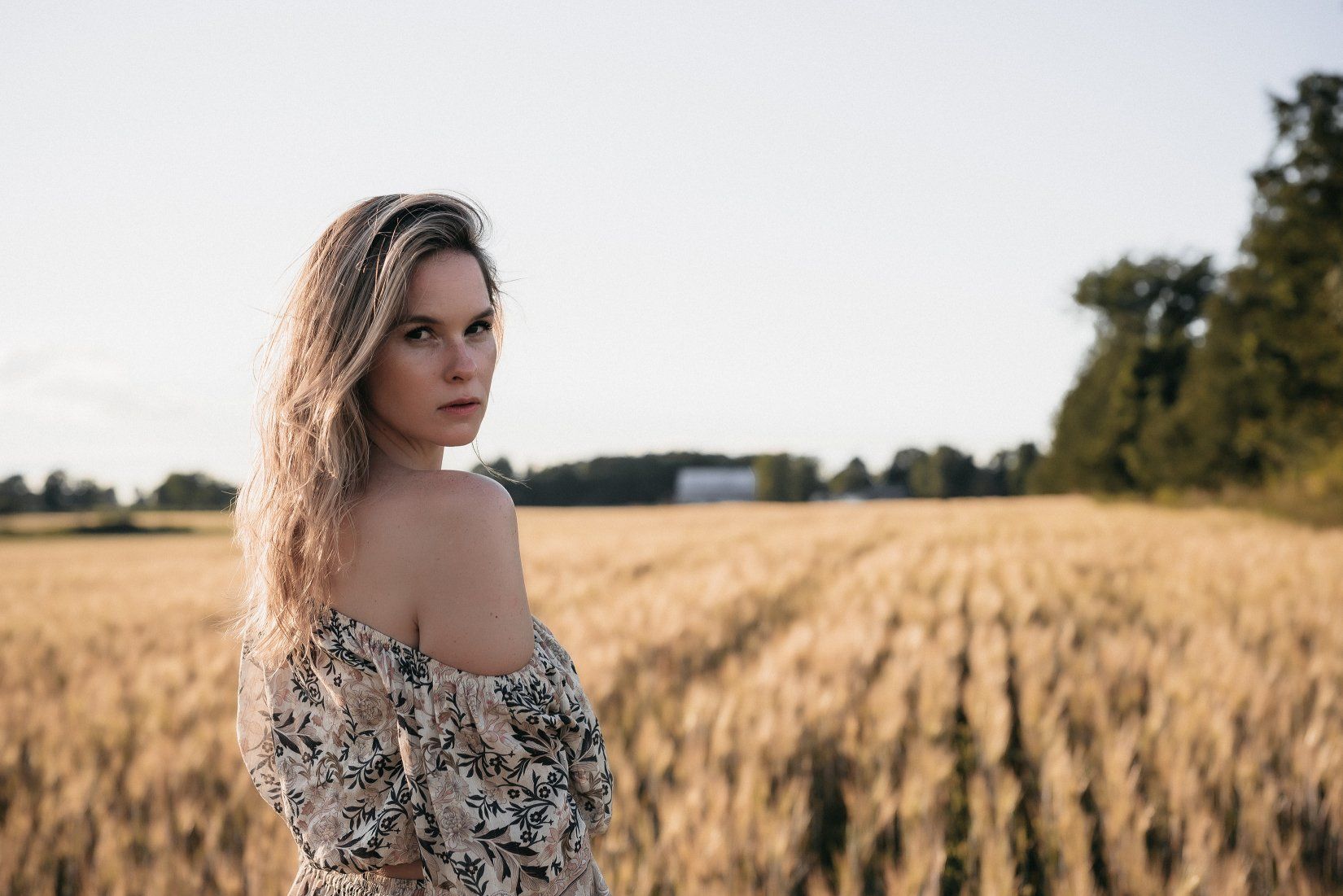 Personal branding photo of a blond woman looking back over her bare shoulder while standing in front of a field
