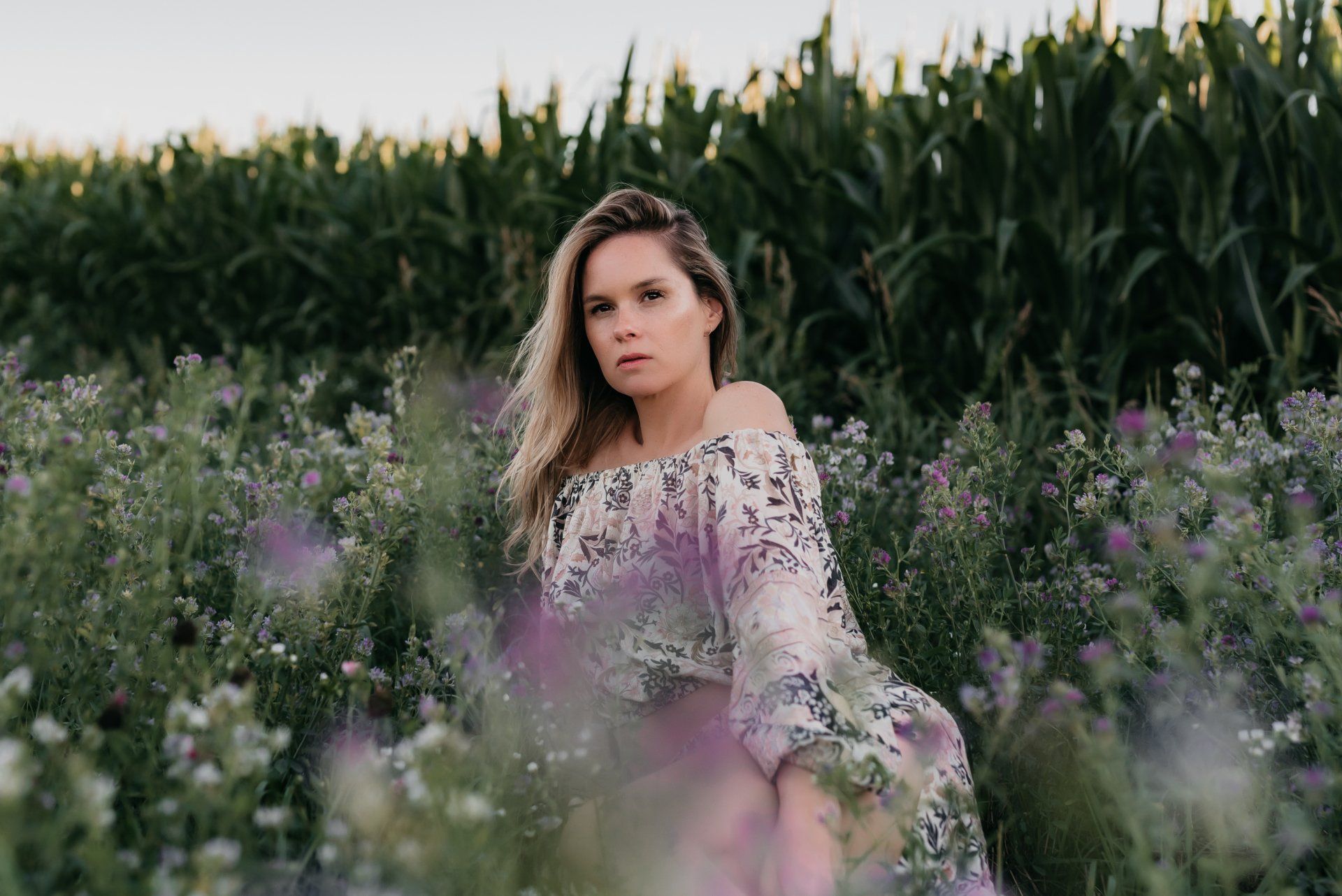 Personal branding photo of a blond woman wearing a flower blouse while standing in a field of tall wild flowers