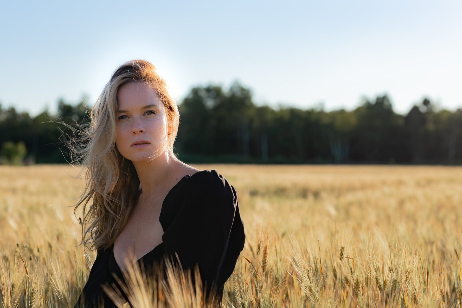 Personal branding photo of a woman with long blond hair wearing a black top standing in a field of golden wheat