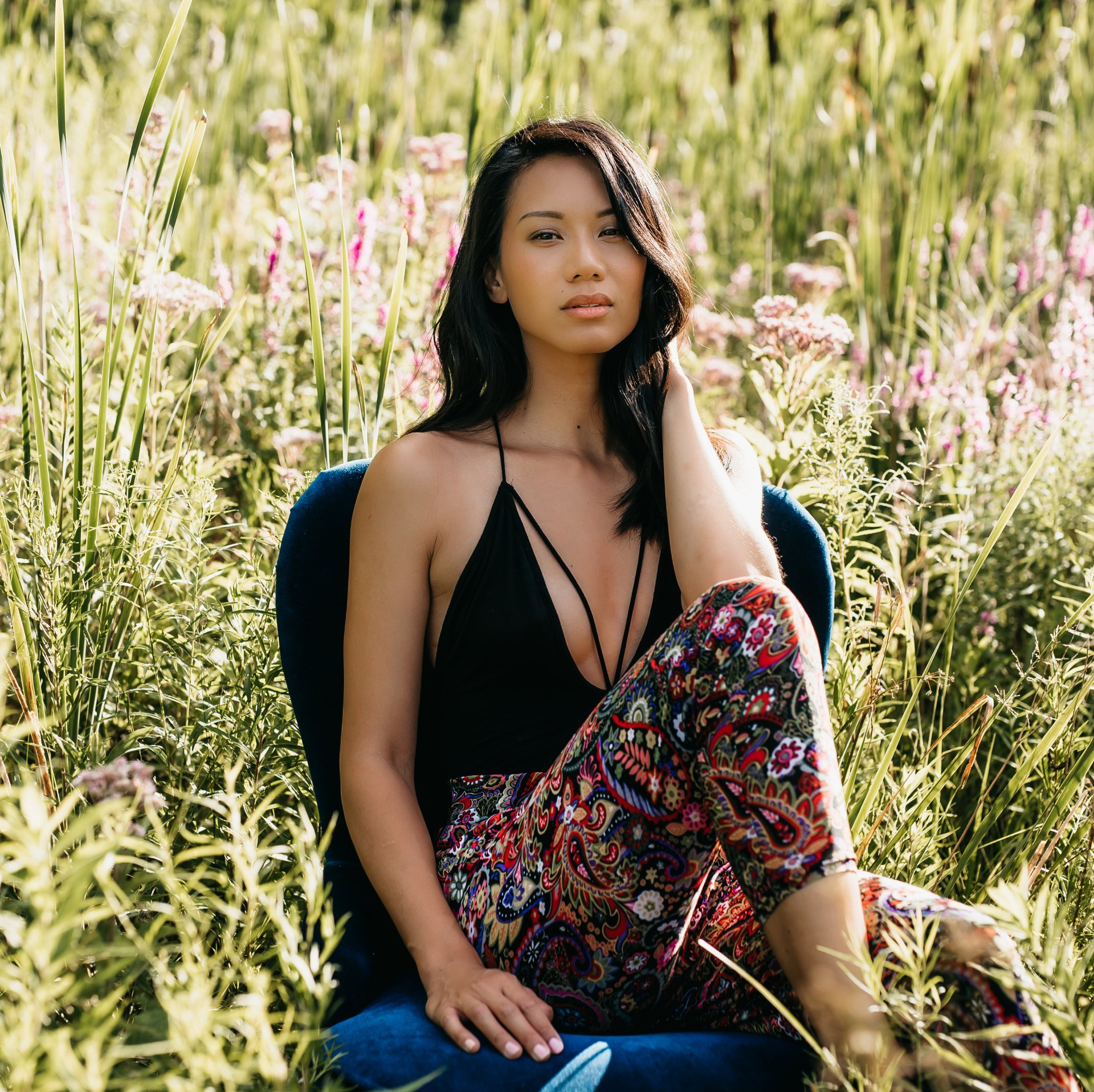 Personal branding photograph of a young lady with long black hair sitting in field with tall grasses and wild flowers