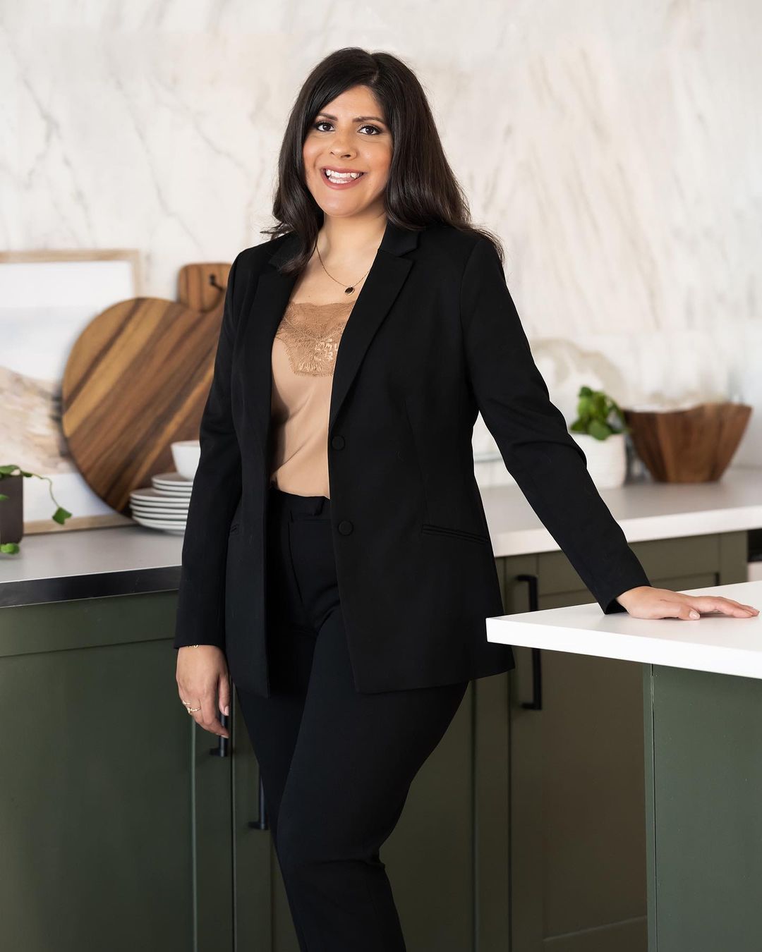 woman with black suit and golden brown top posing in the kitchen