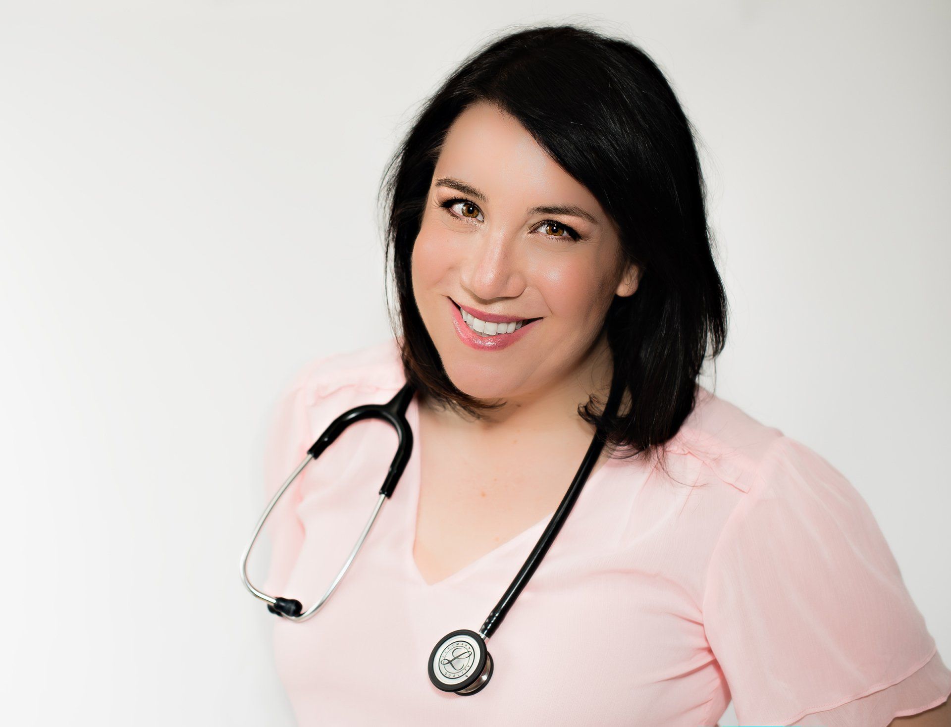 A female physician with a stethoscope draped over her shoulder smiles and tilts her head slightly to the side.