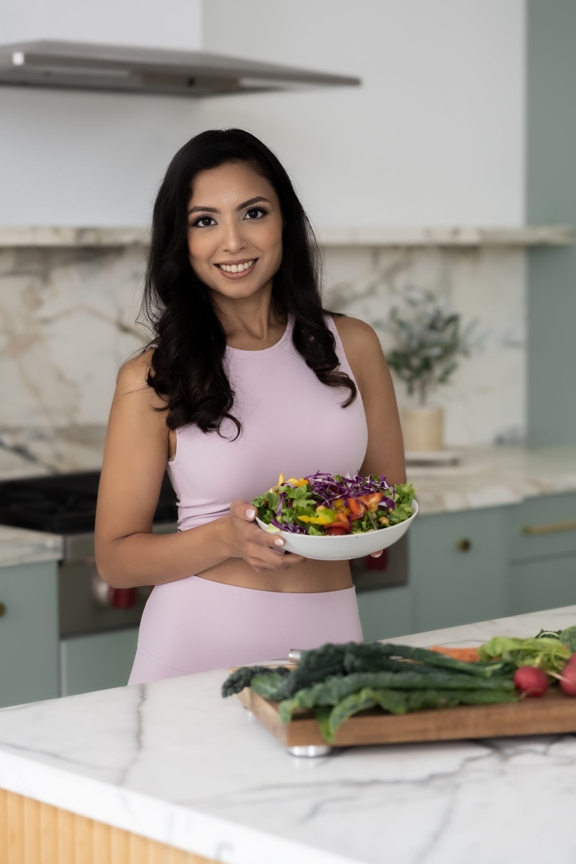 A woman is holding a bowl of salad in a kitchen.