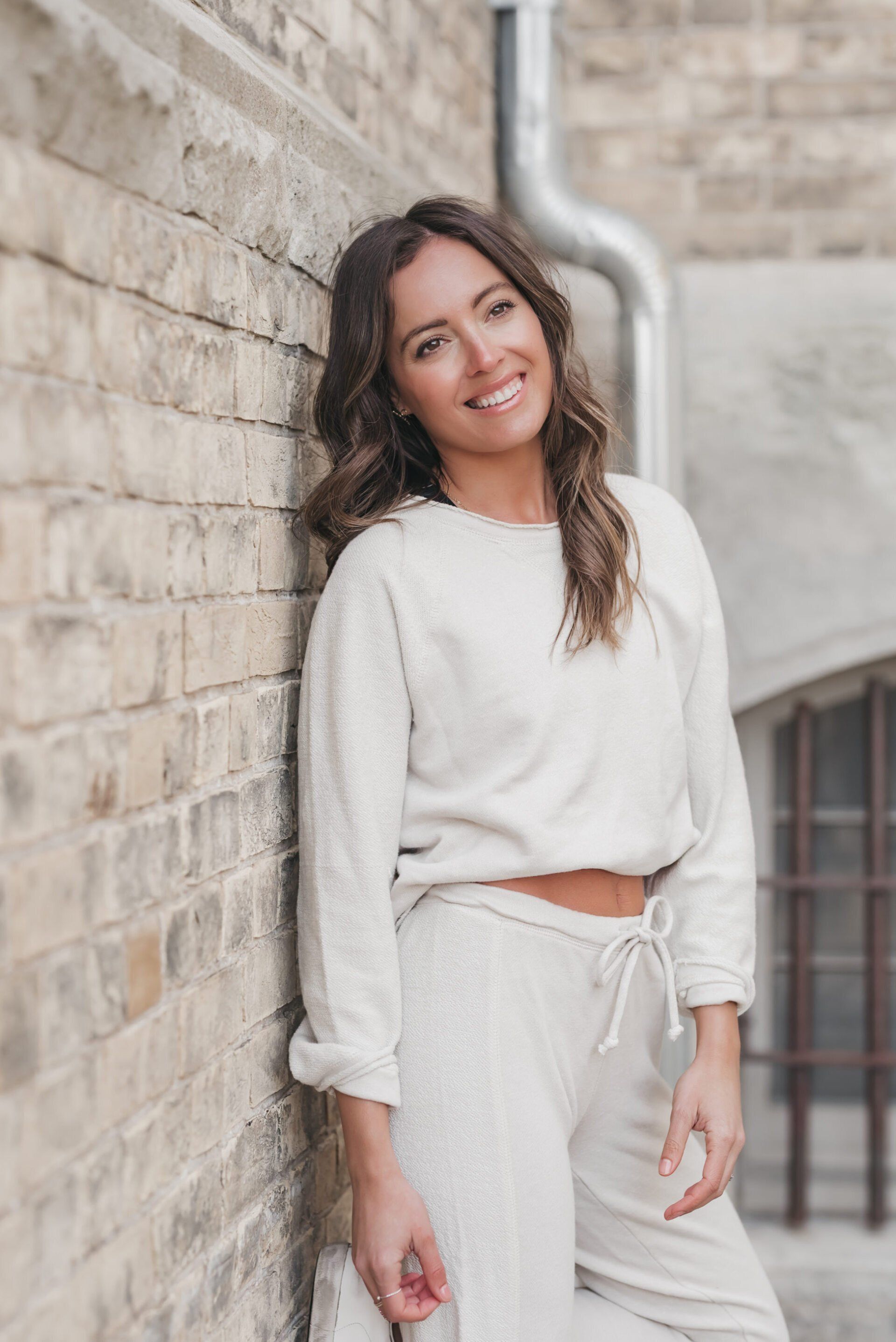 a woman wearing white coords while leaning on a brick wall