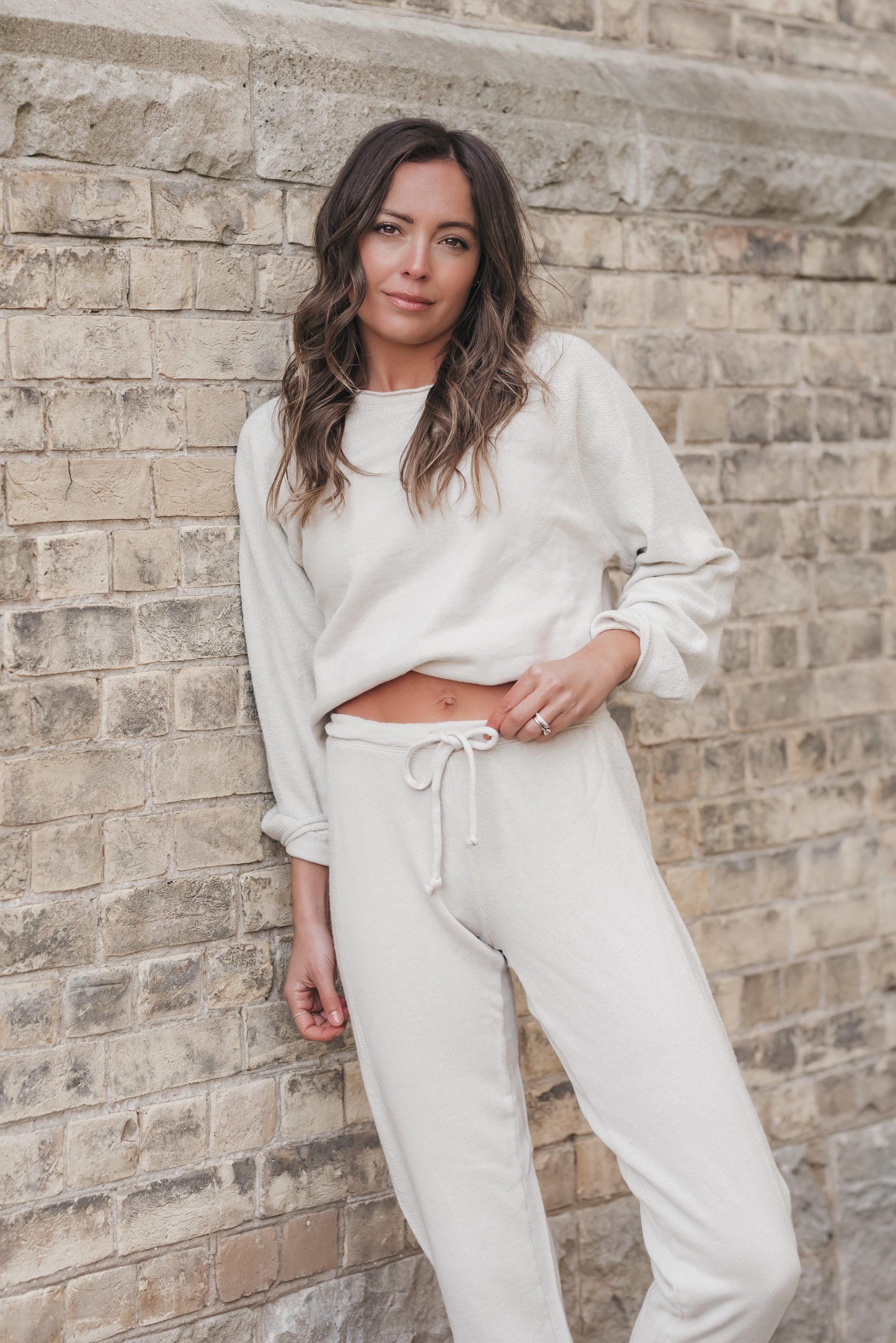 a woman leaning on a beige brick wall