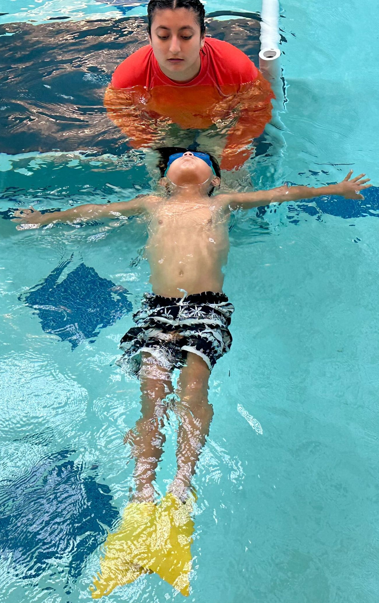 A woman is teaching a young boy how to swim in a swimming pool.