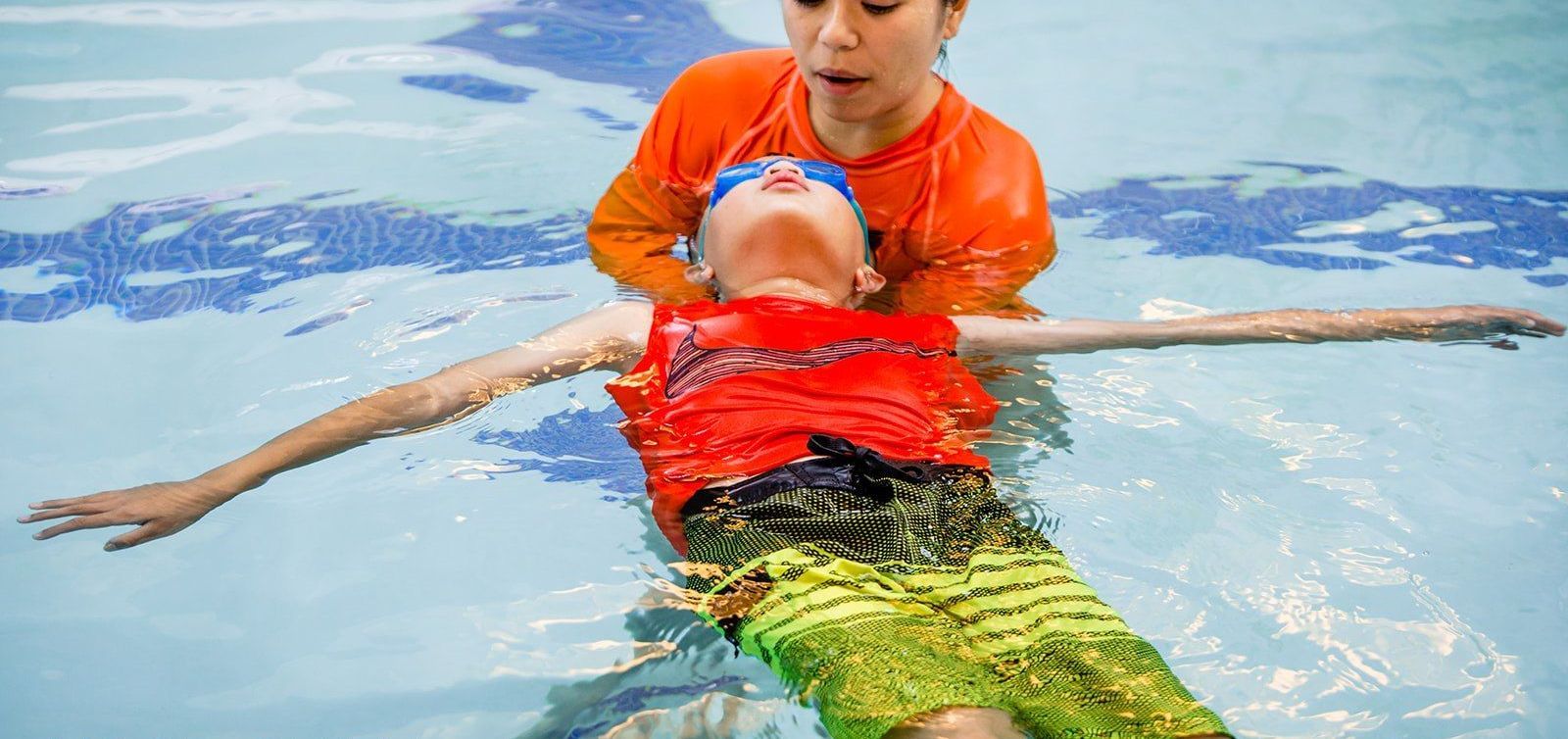 A woman is teaching a young boy how to swim in a swimming pool.