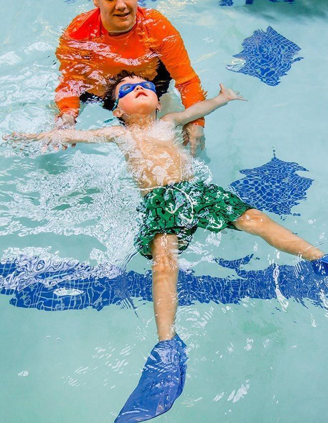 A woman is teaching a young boy how to swim in a swimming pool.