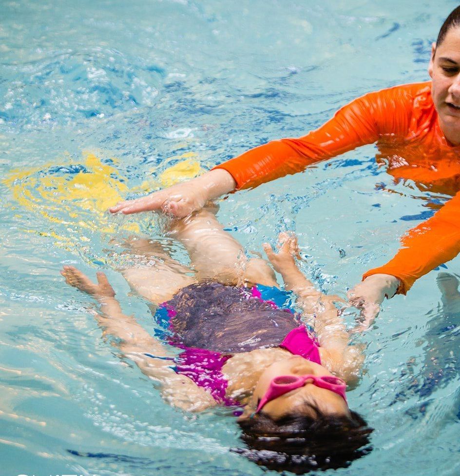 A man is teaching a little girl how to swim in a swimming pool.