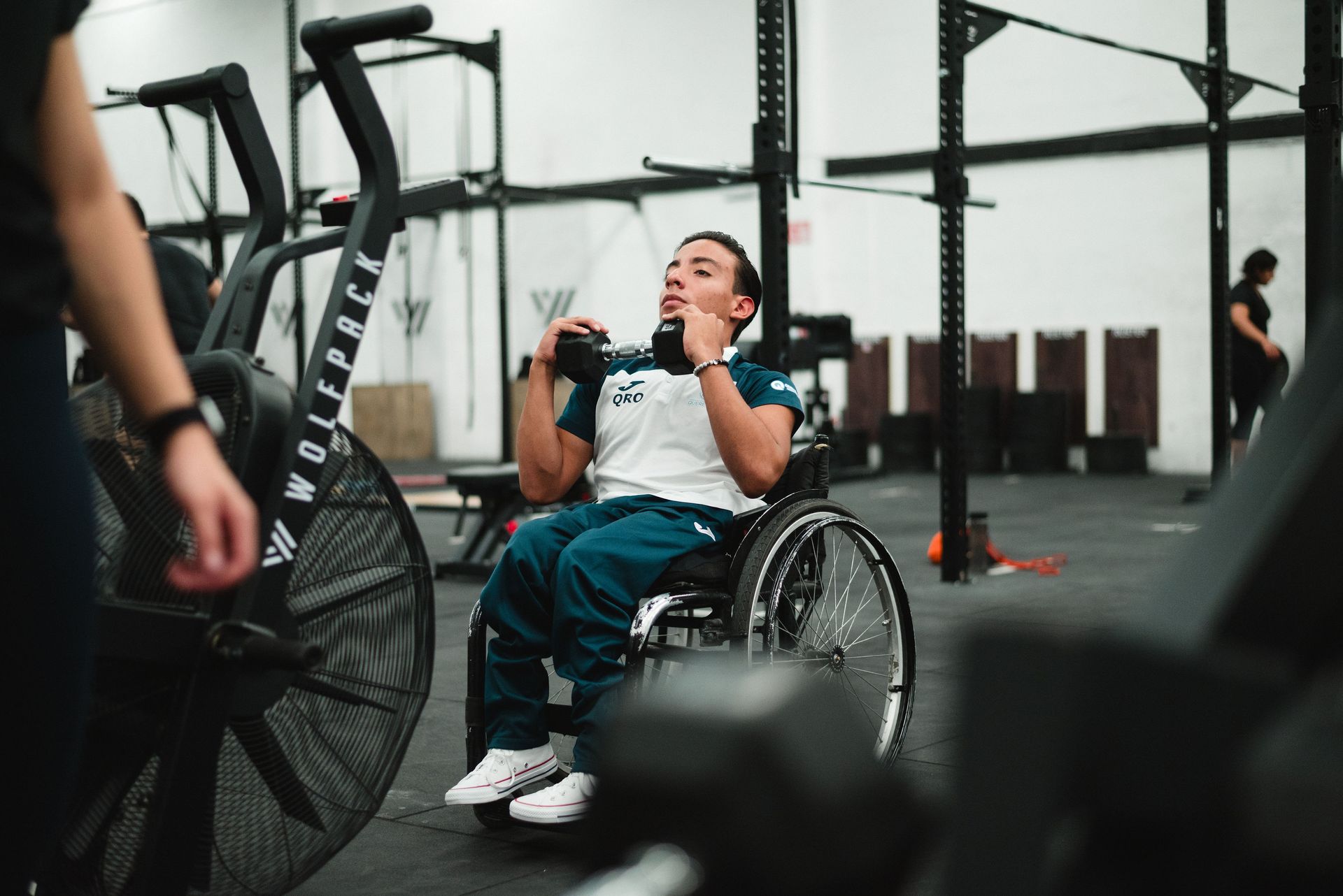 Hombre en silla de ruedas haciendo ejercicio con mancuernas en un gimnasio.