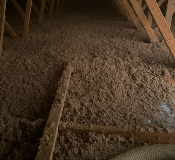 Vue de l'intérieur d'un grenier avec isolation en cellulose brune entre des chevrons en bois.