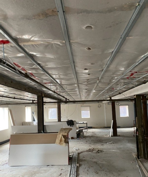 Intérieur d'un bâtiment en construction ; poutres apparentes au plafond, charpentes métalliques et isolation.