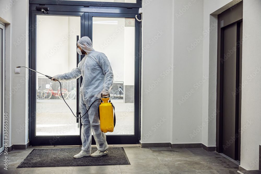 A man in a protective suit is spraying a door with a sprayer.