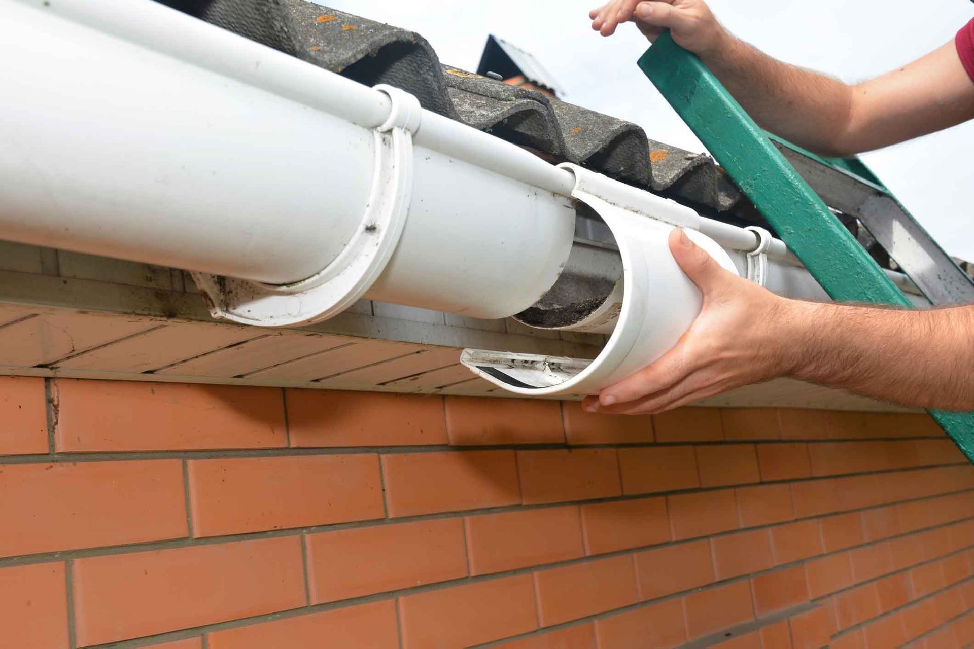 A person is installing a gutter on a brick wall.