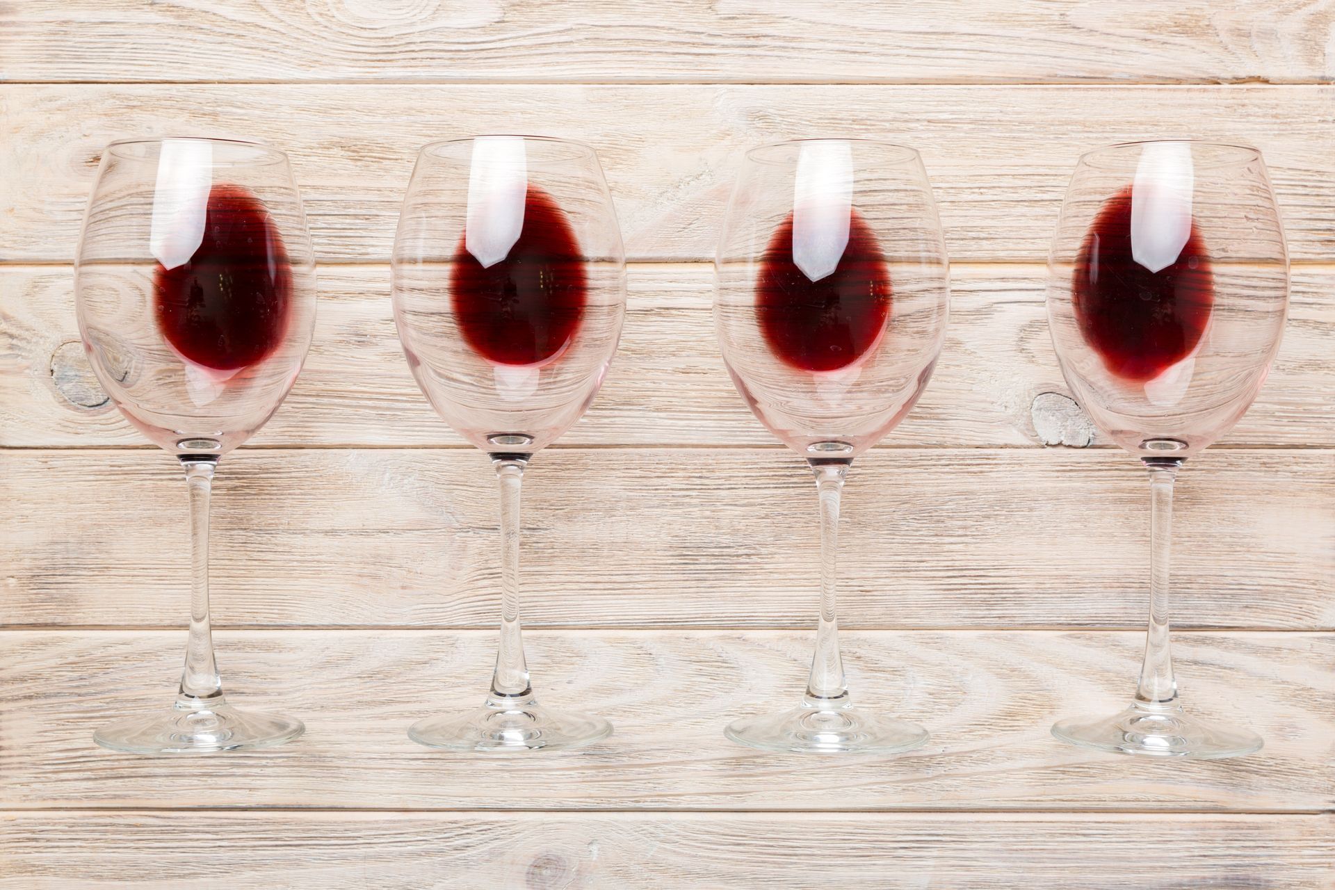 Four wine glasses filled with red wine on a wooden table.